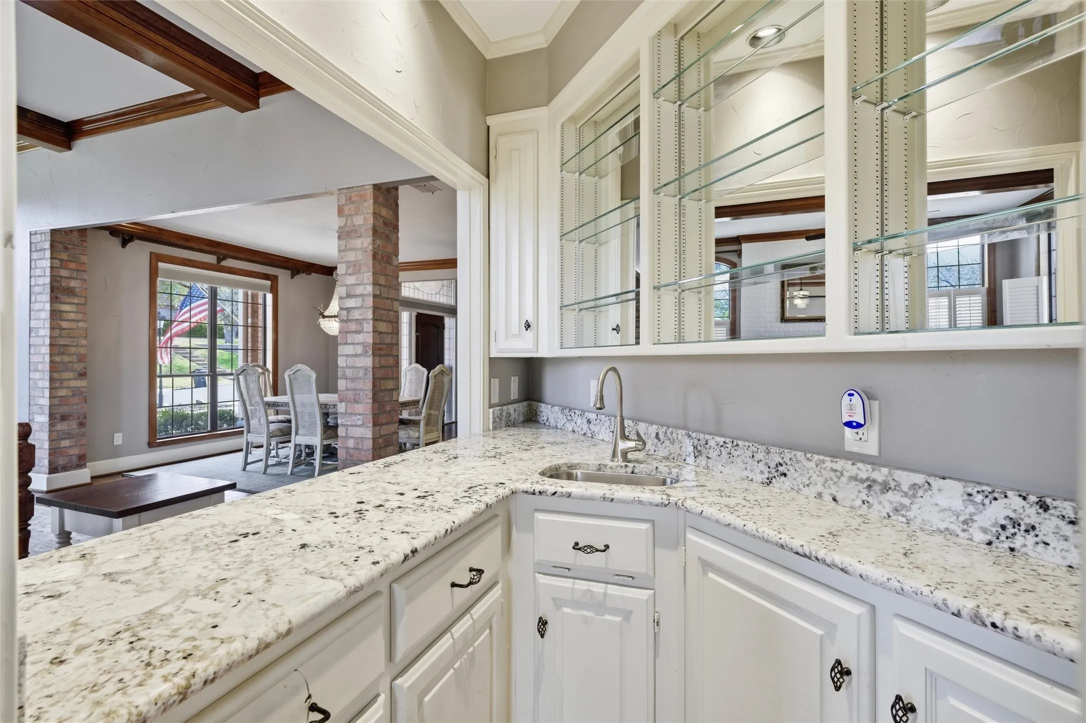 Wet Bar featuring ornamental molding, decorative columns, light stone countertops, and white cabinets