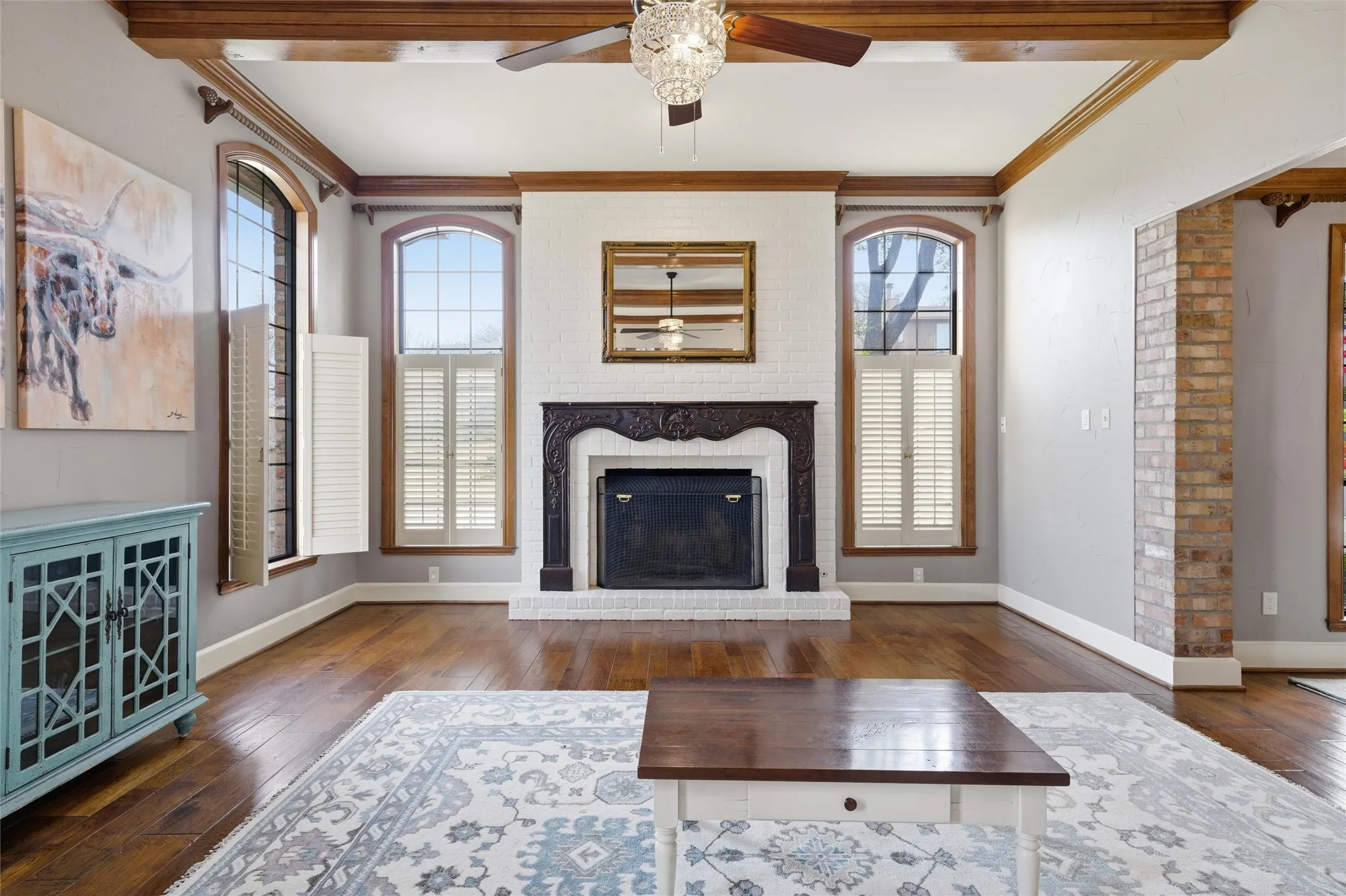 Unfurnished living room featuring ornamental molding, a fireplace, a ceiling fan, dark wood-style floors, and beamed ceiling