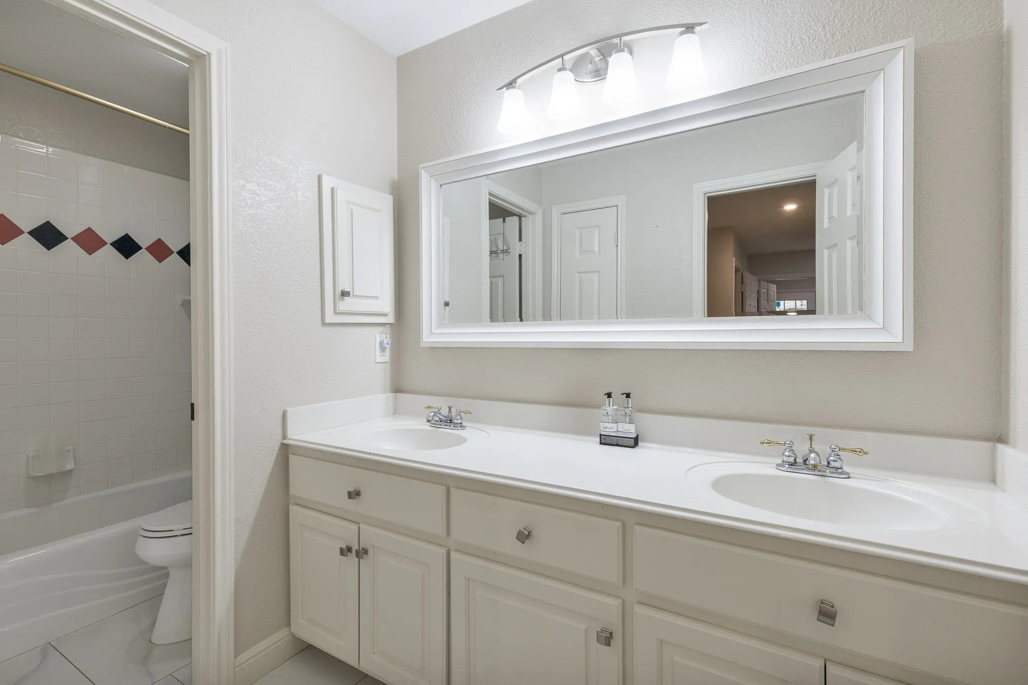 Bathroom with double vanity, shower / tub combination, and a textured wall