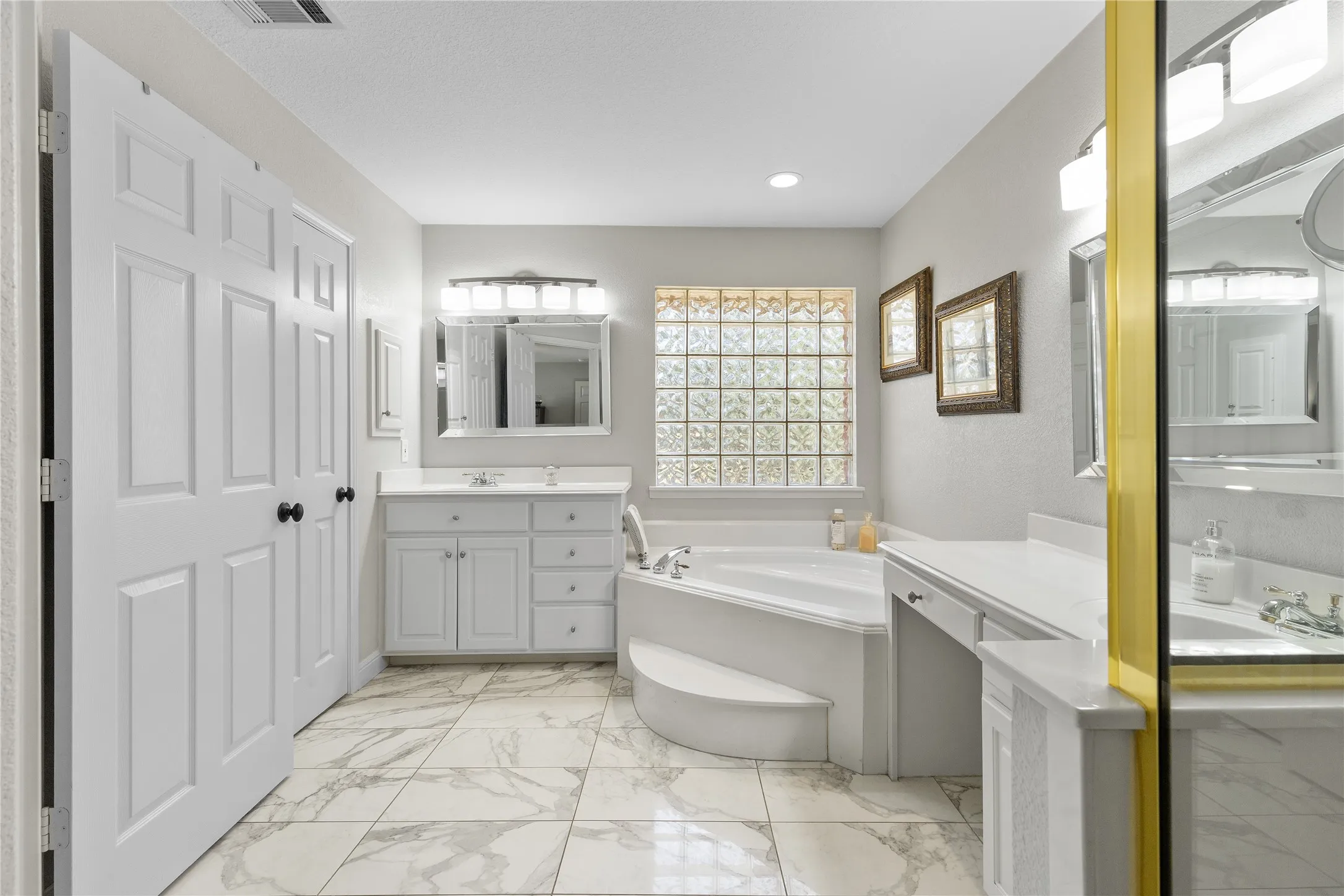 Bathroom featuring a garden tub, light marble finish floors, and two vanities