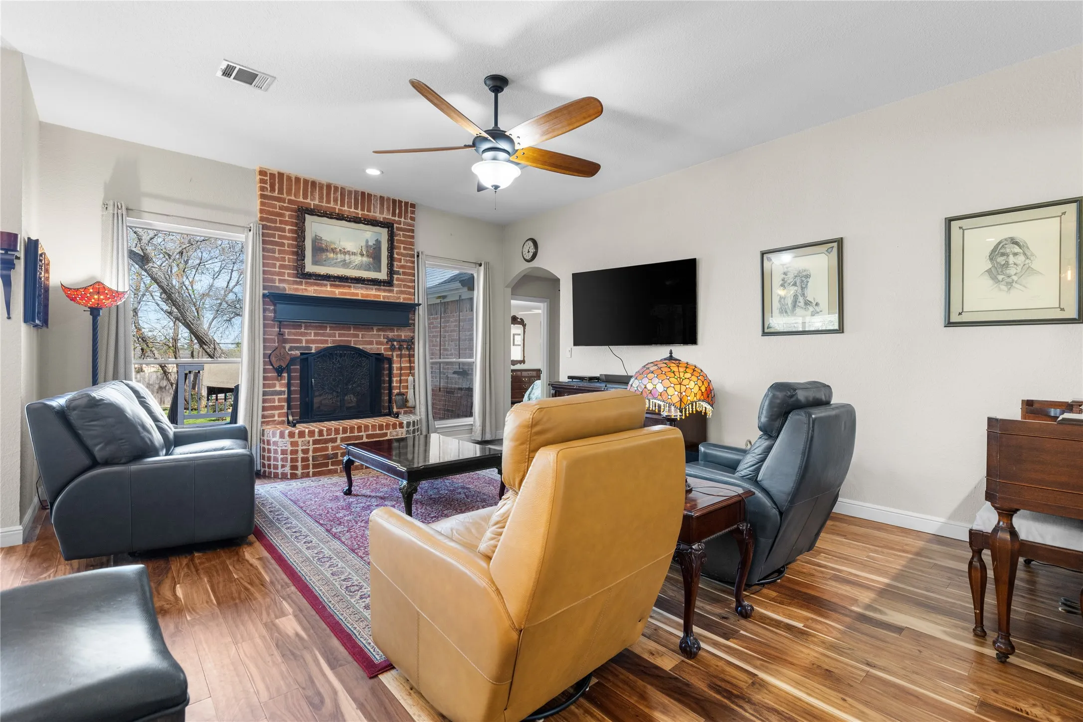 Living room with wood finished floors, a brick fireplace, and plenty of natural light