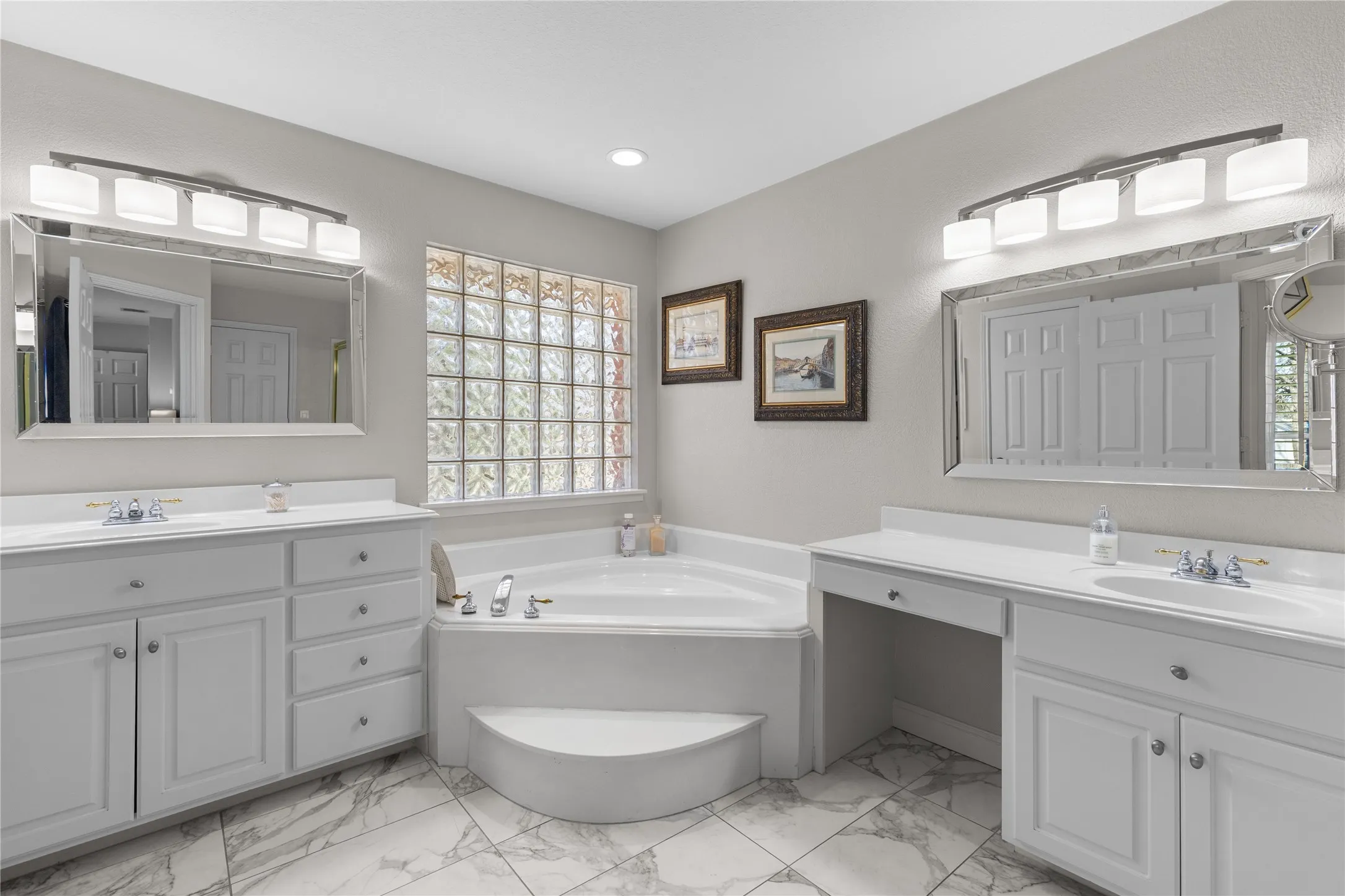 Full bath featuring two vanities, a garden tub, and light marble finish flooring
