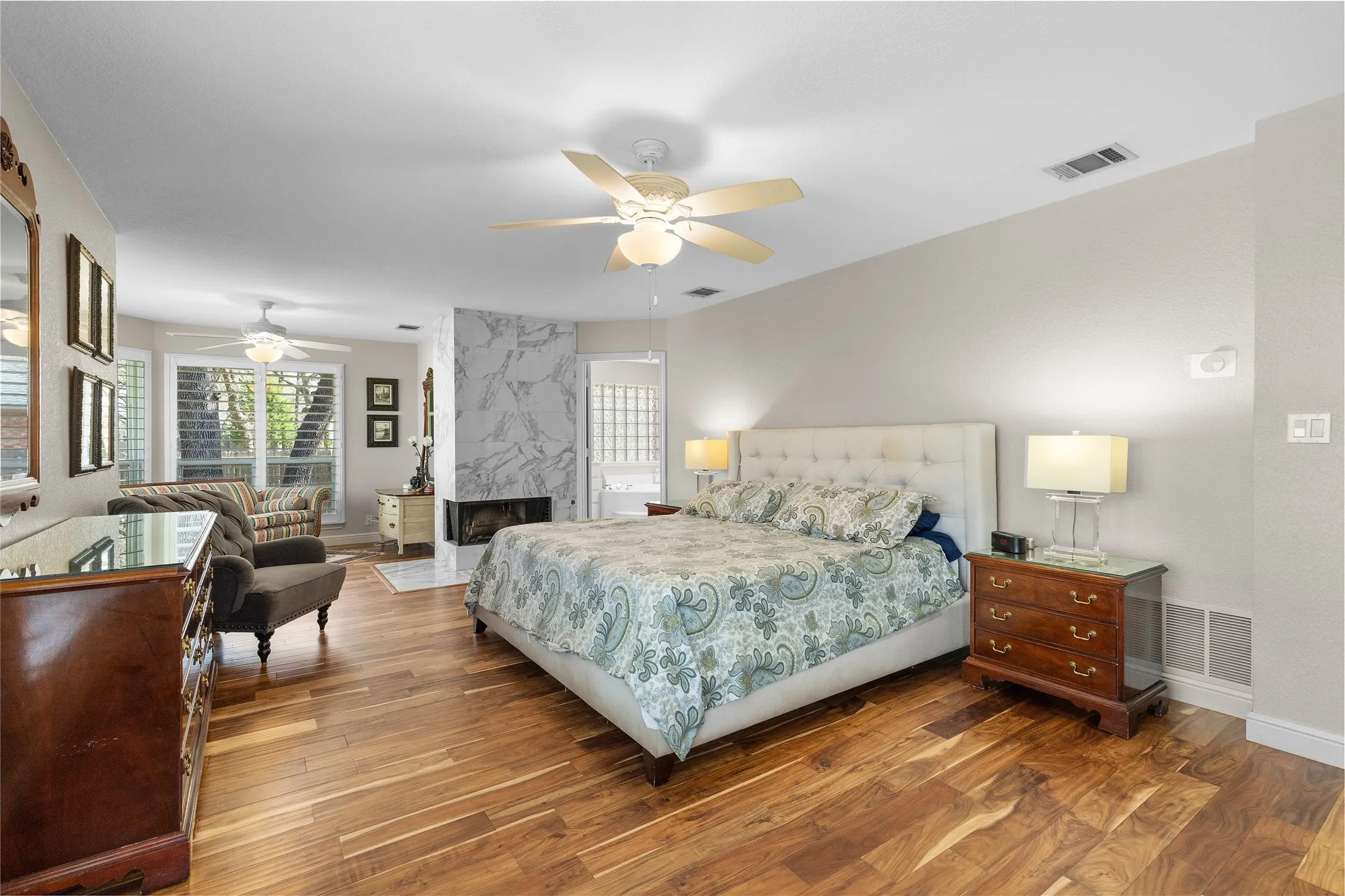 Bedroom with dark wood finished floors, ceiling fan, and a high end fireplace