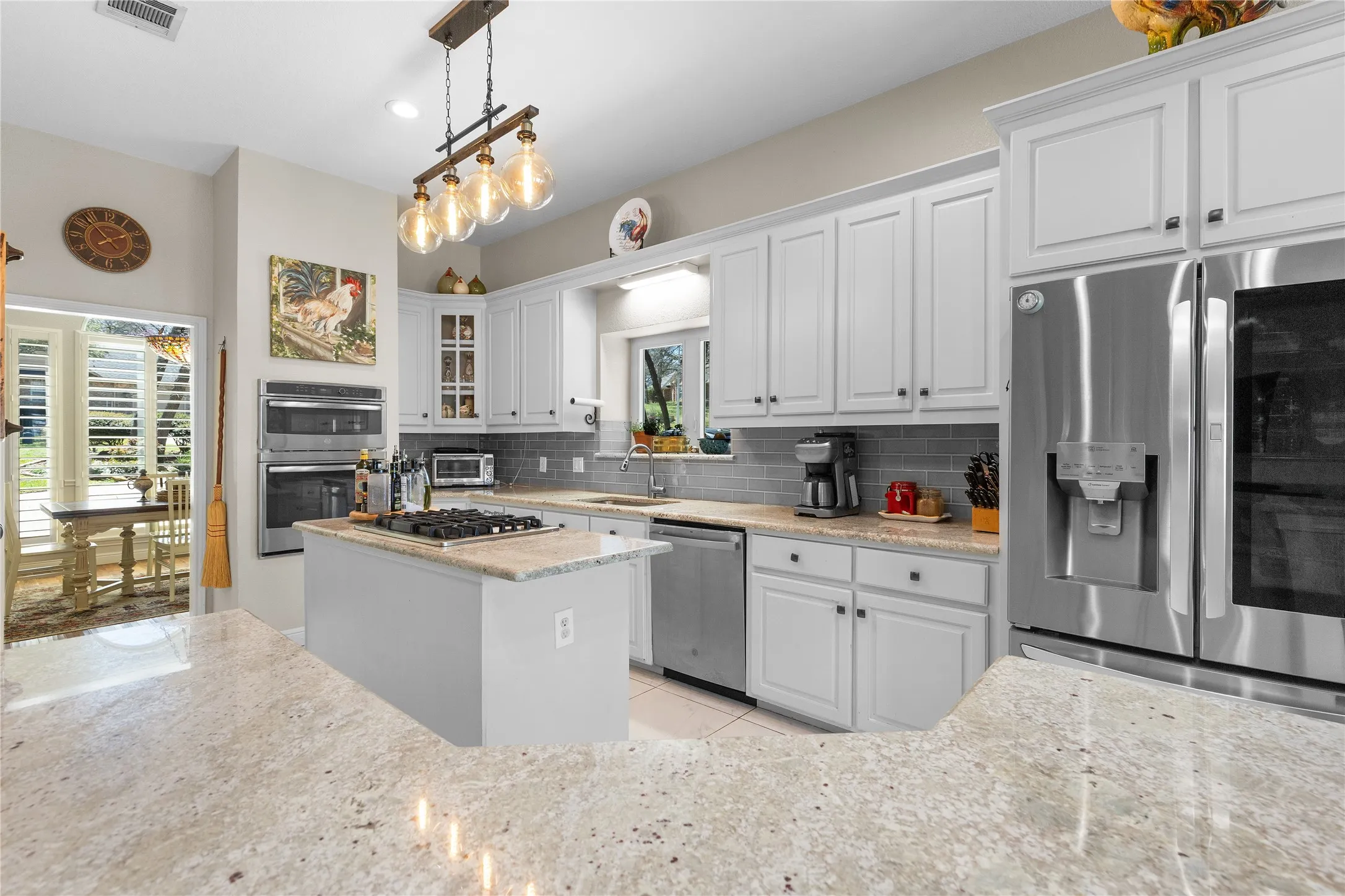 Kitchen with stainless steel appliances, white cabinetry, glass insert cabinets, light stone countertops, and a kitchen island