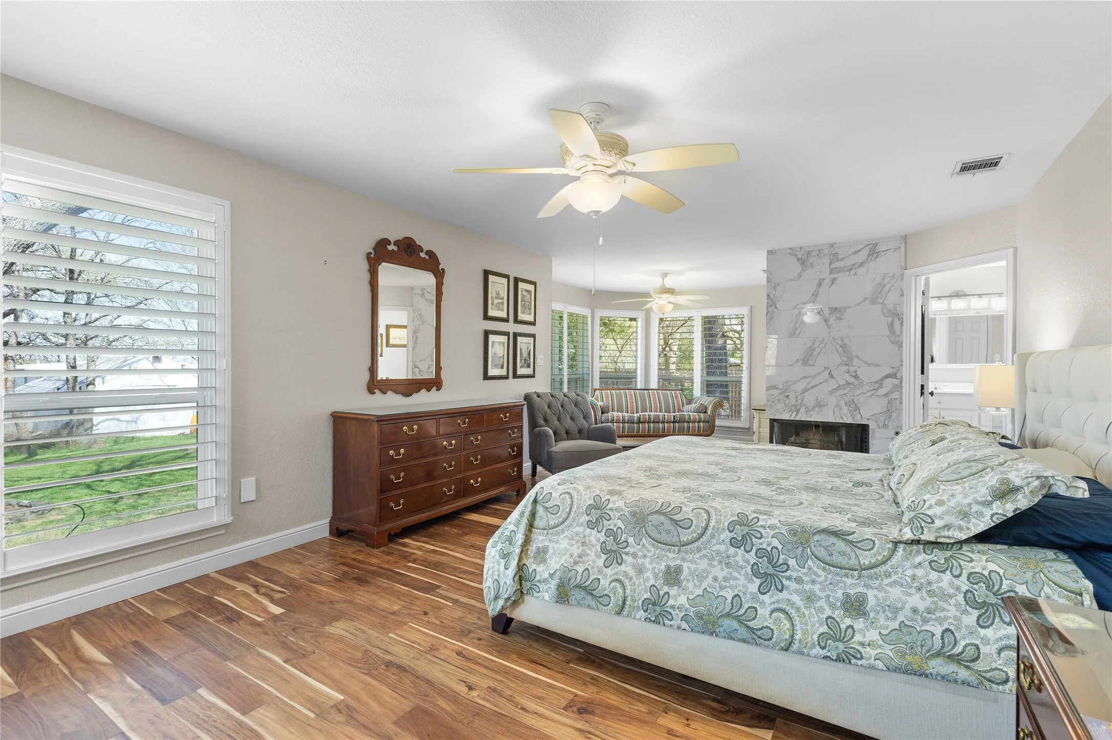 Bedroom featuring connected bathroom, dark wood-style flooring, a fireplace, and ceiling fan