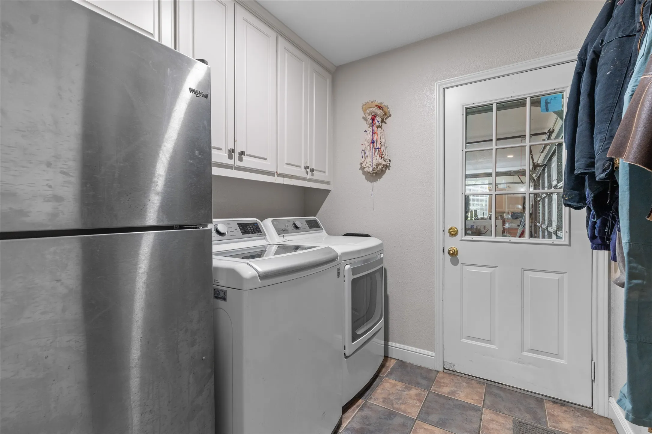 Laundry room featuring washing machine and dryer, refrigerator, stone finish floors, and a textured wall