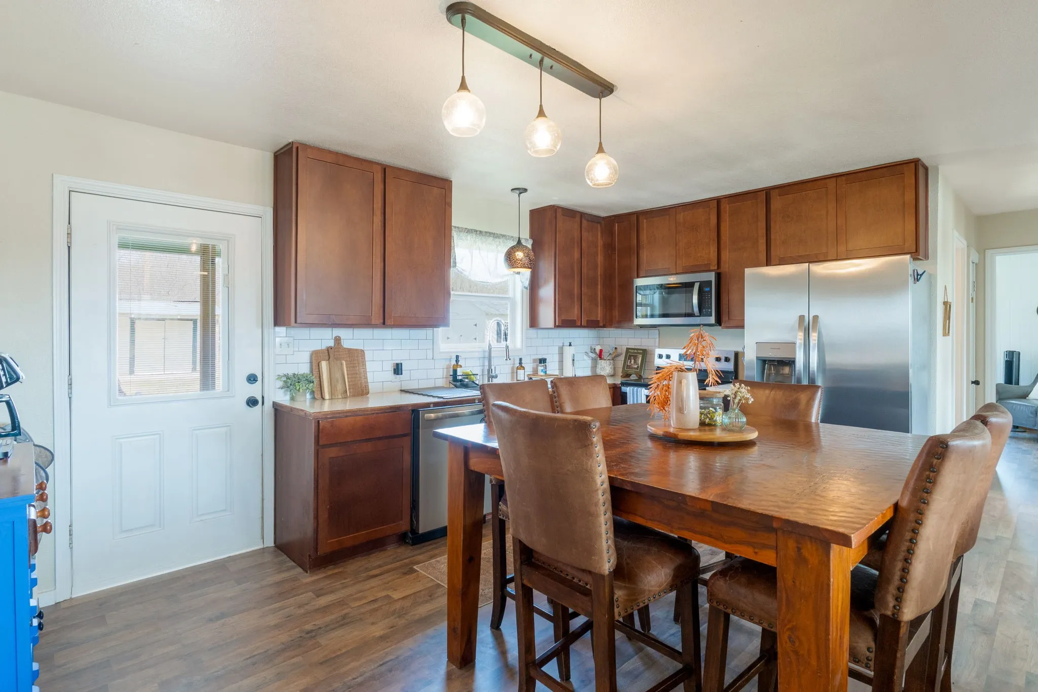 Kitchen with wood finish cabinetry, stainless steel appliances, pendant lighting, light countertops, and dark wood-type flooring