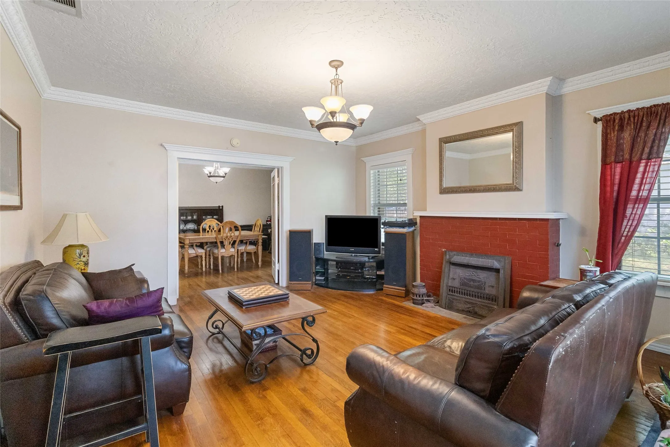 Living room featuring hanging lights, wood finished floors, a fireplace, a textured ceiling, and crown molding