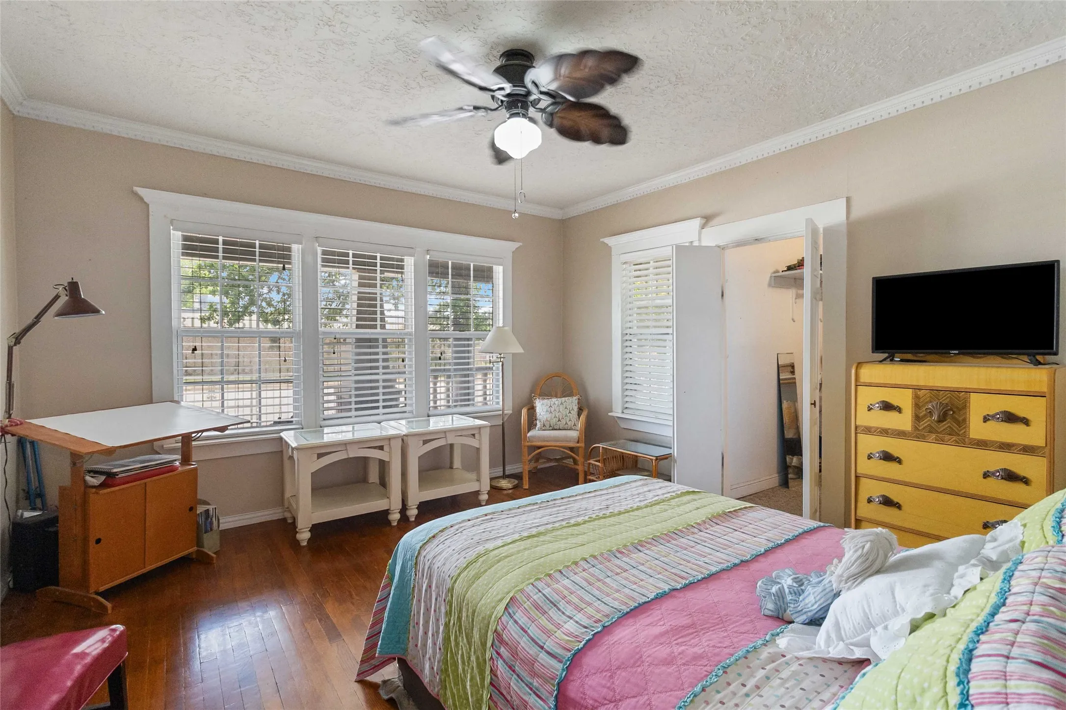 Bedroom with a walk in closet, wood-type flooring, a ceiling fan, ornamental molding, and a textured ceiling