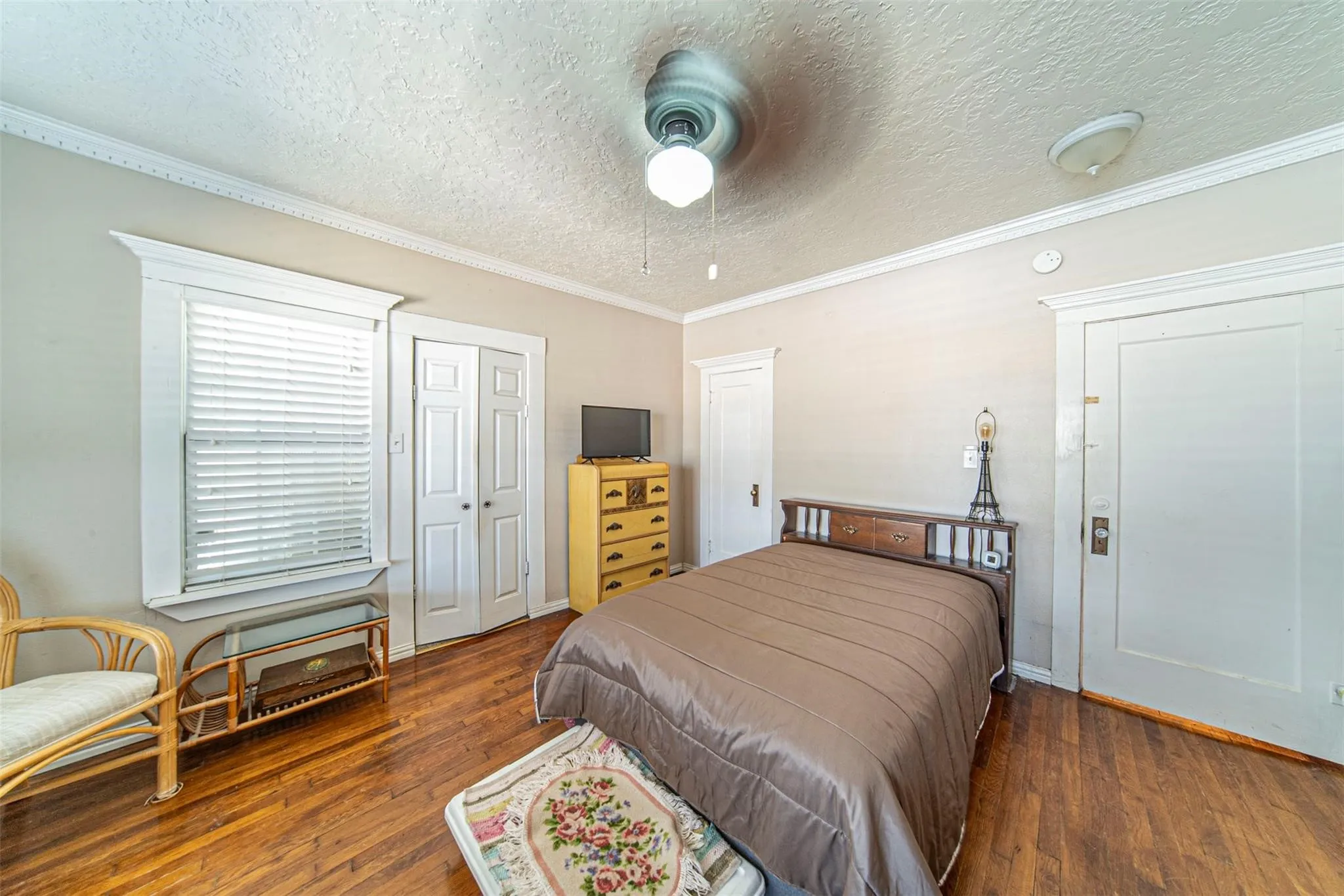 Bedroom featuring a closet, a textured ceiling, ornamental molding, wood finished floors, and a ceiling fan