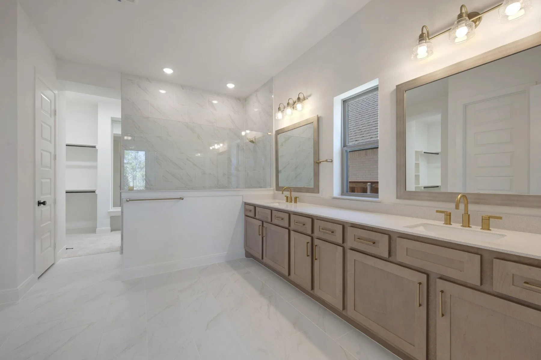 Spacious bathroom featuring a dual vanity with light wood-finish cabinetry and gold-tone hardware, white countertops, and dual mirrors