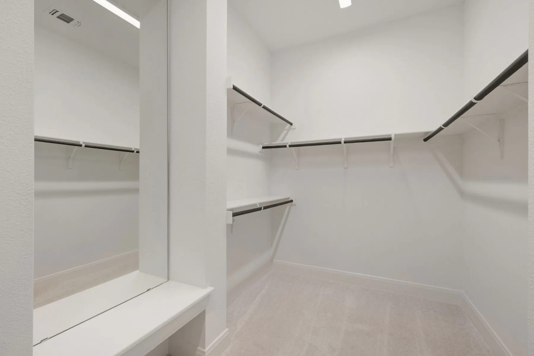 Walk-in closet featuring light-toned carpeting, white walls, multiple shelving units, and hanging rods