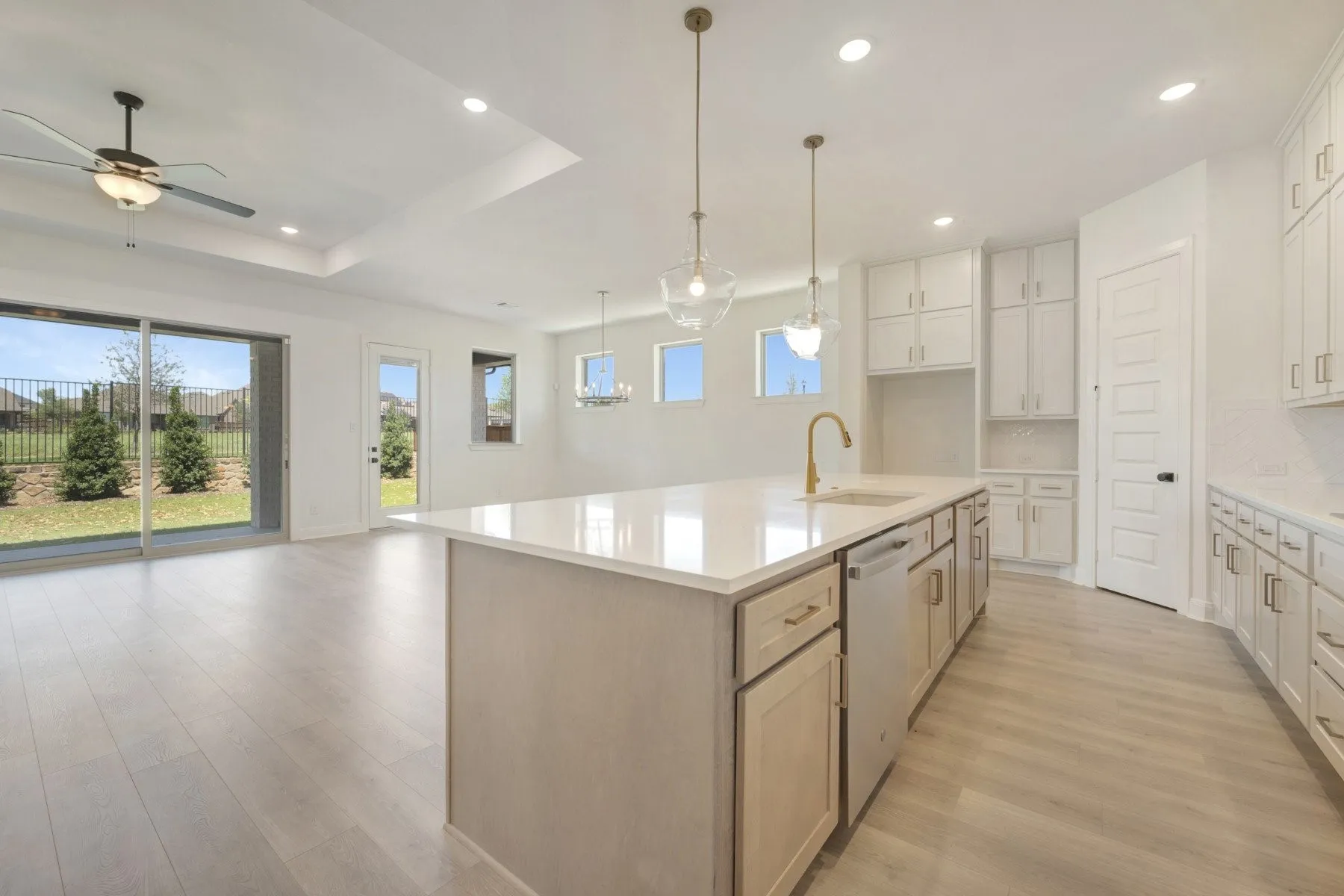 Open-concept kitchen and living area featuring light wood-finish flooring, a kitchen island with a white countertop and integrated sink, pendant lighting, white cabinetry, and sliding glass doors to the exterior