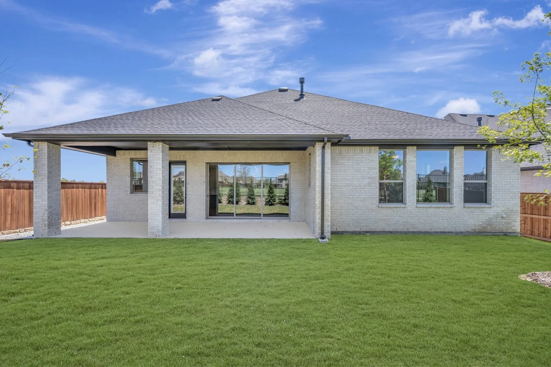 Expansive backyard featuring a manicured lawn, a covered patio with block columns, and a full-light rear entry door