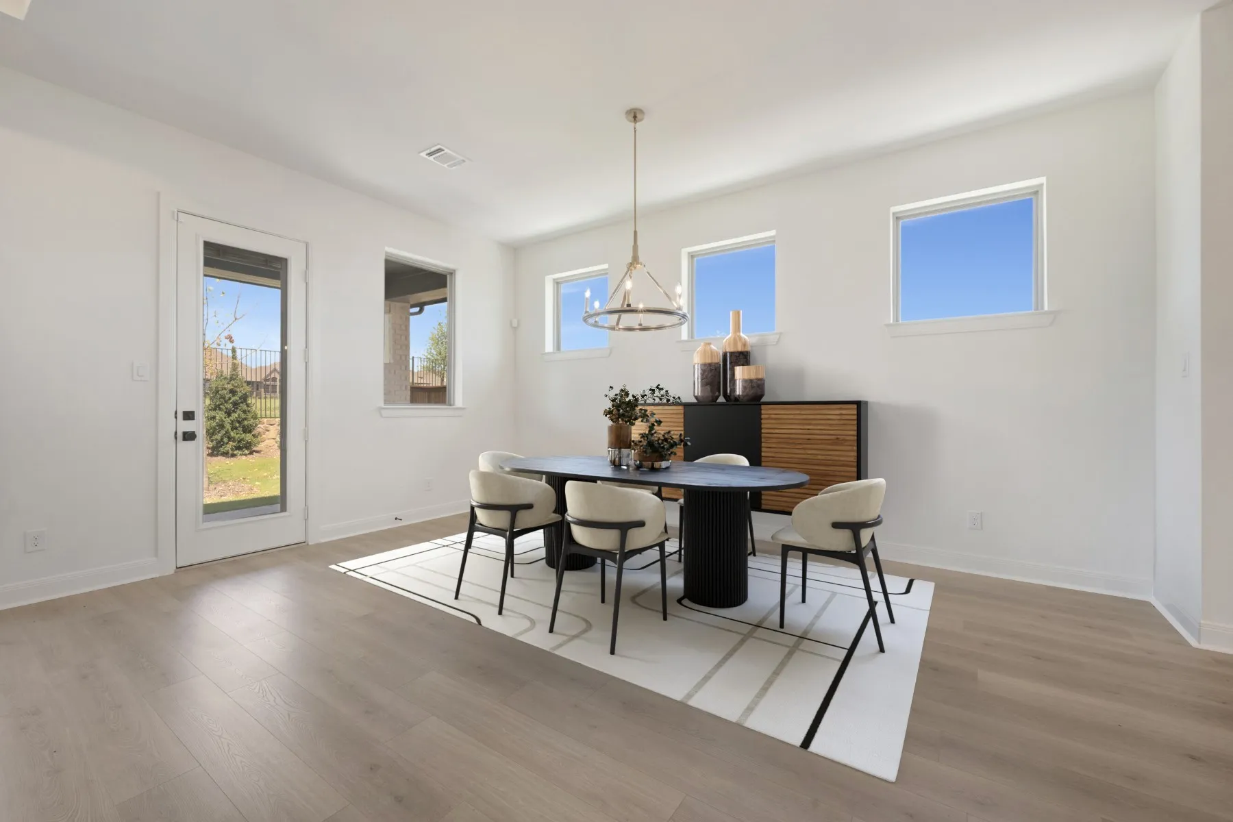 Spacious room featuring light wood-finish flooring, multiple windows, a glass-paneled exterior door, and a suspended chandelier