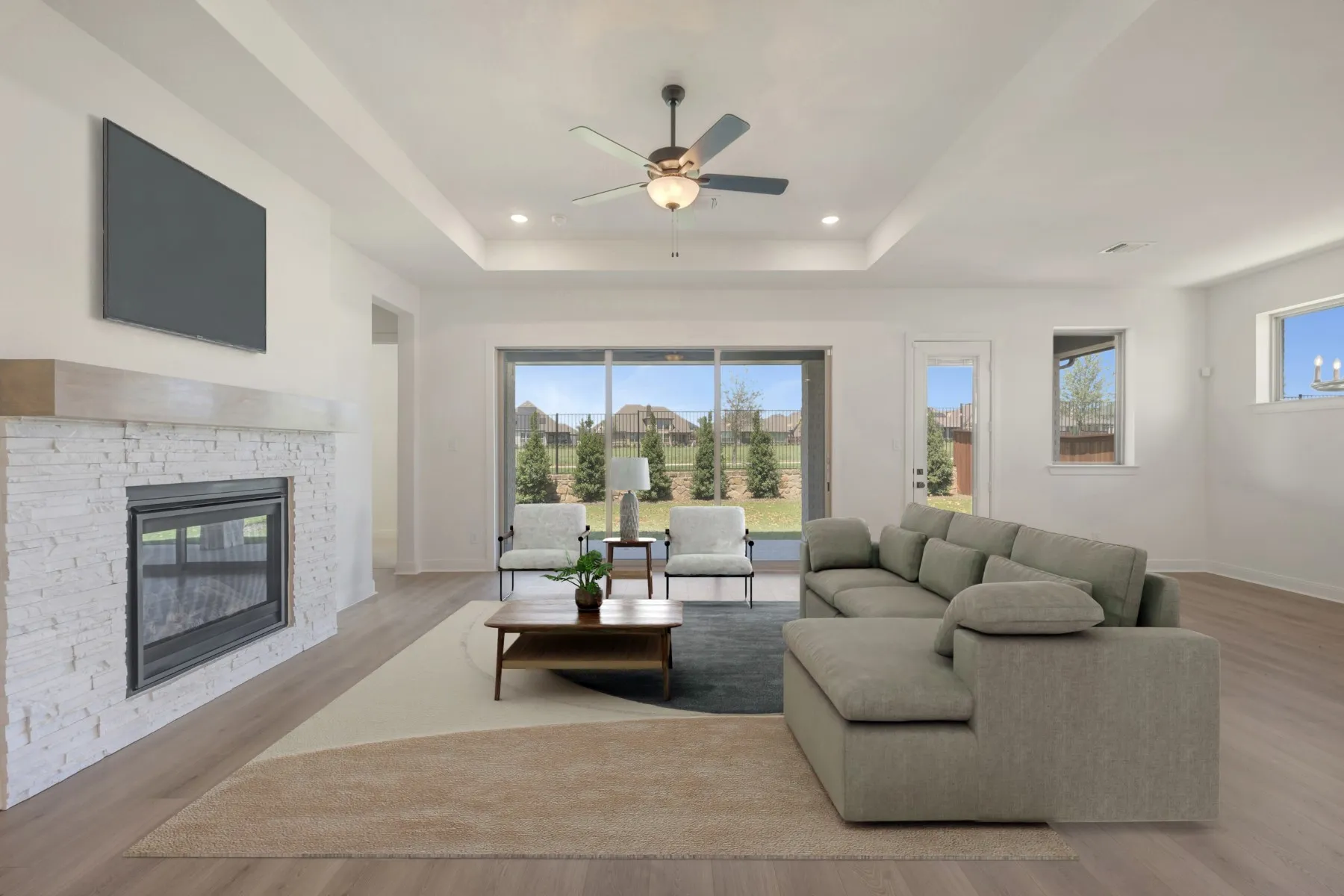 Spacious living area featuring a stone-clad fireplace with a wood mantel, a ceiling fan with integrated lighting, and a tray ceiling