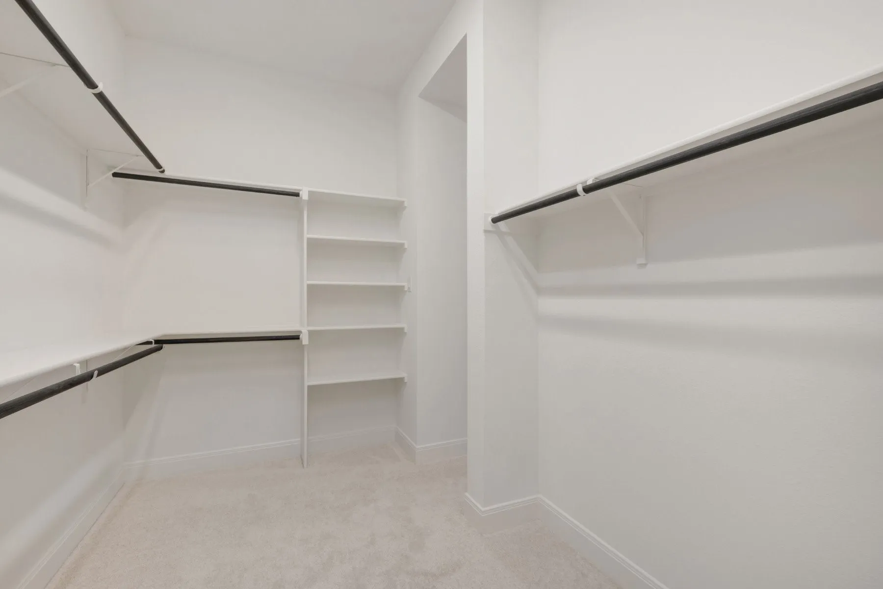 Walk-in closet featuring built-in shelving, multiple hanging rods, and light-toned carpeting