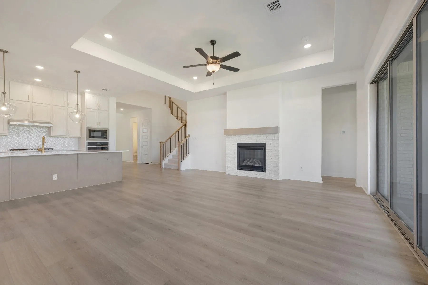 Open-concept living area featuring light wood-finish flooring, a contemporary fireplace with a decorative tile surround and wood mantel, and sliding glass doors