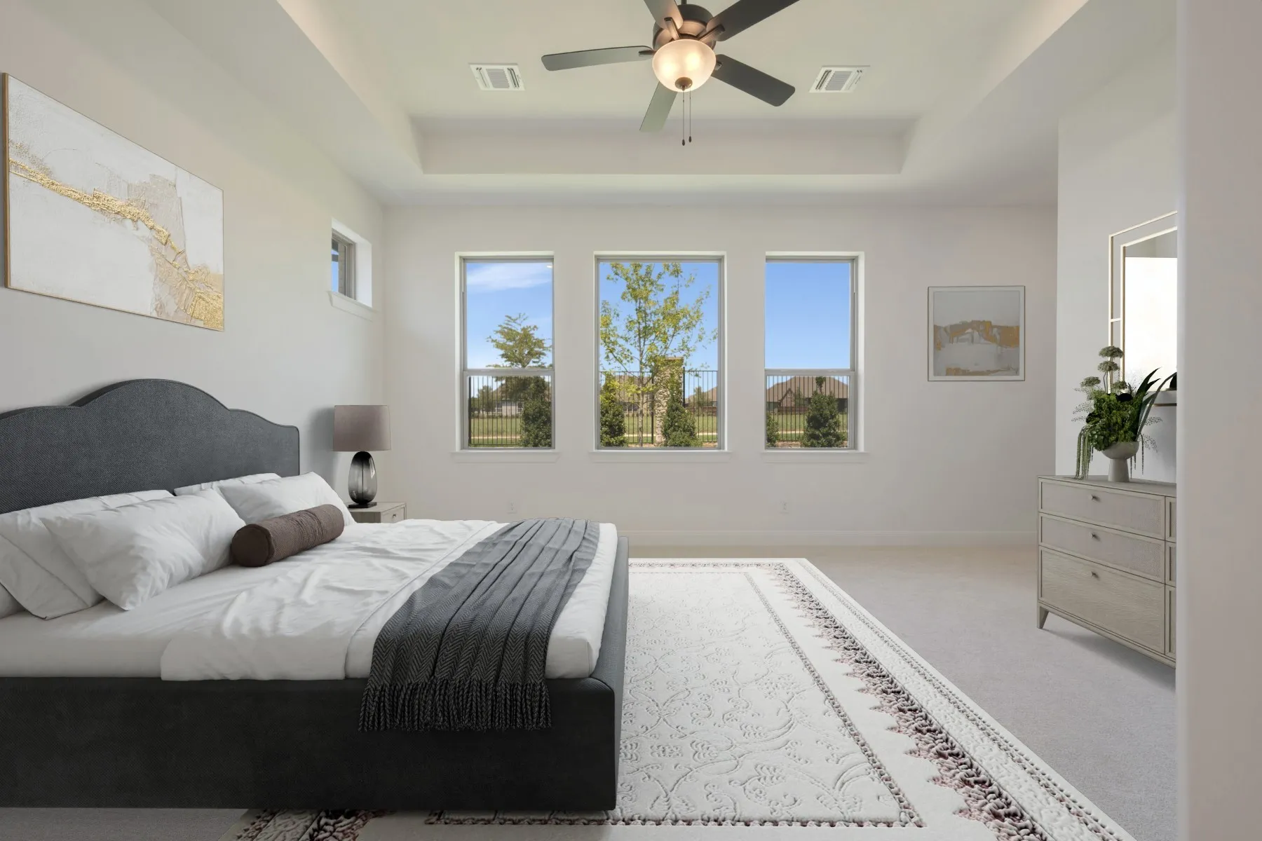 Spacious bedroom featuring a tray ceiling, three large windows, a ceiling fan, and light-toned carpet flooring