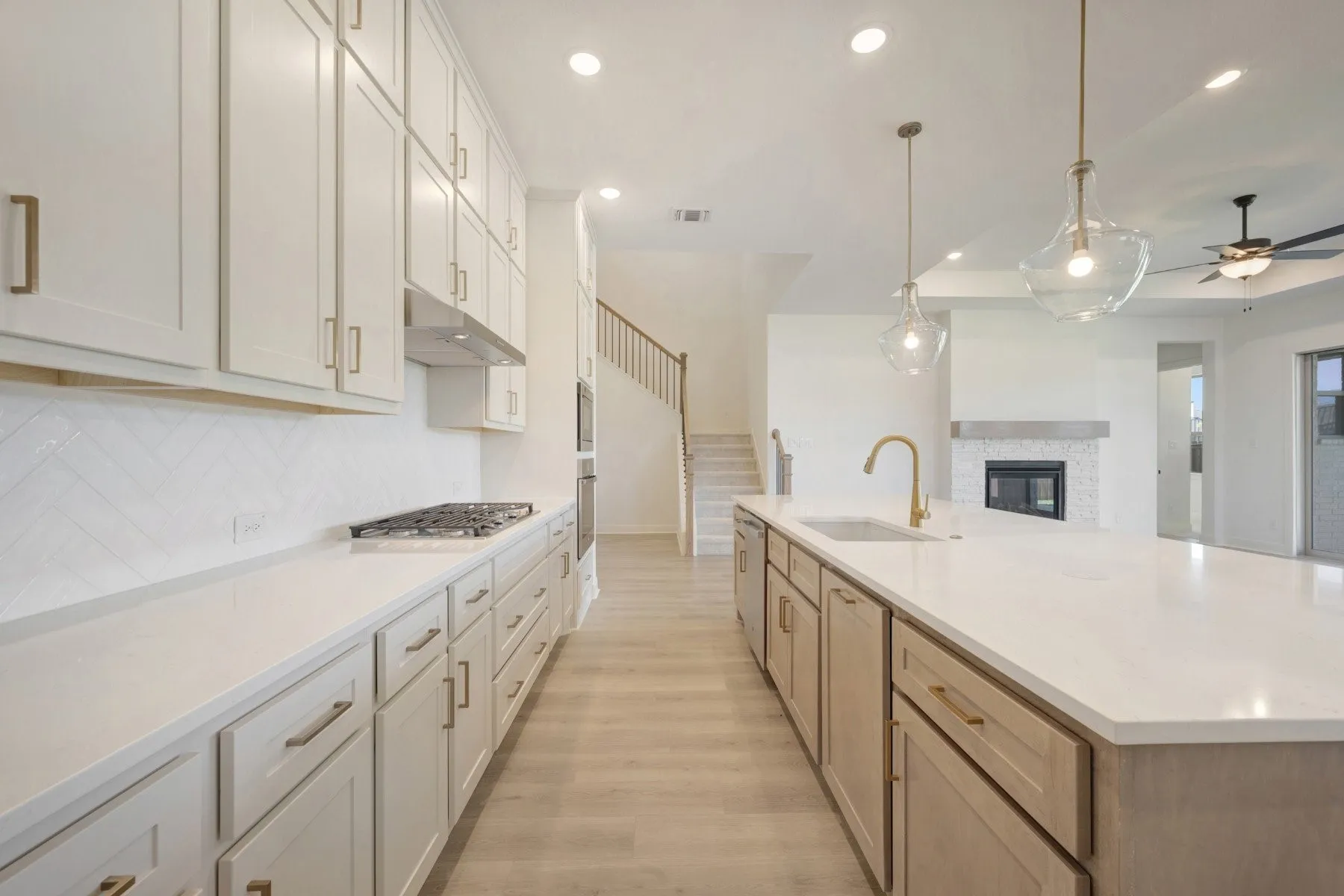 Spacious kitchen featuring a large island with sink, white shaker cabinetry, stainless steel appliances, herringbone tile backsplash, and light wood-finish flooring