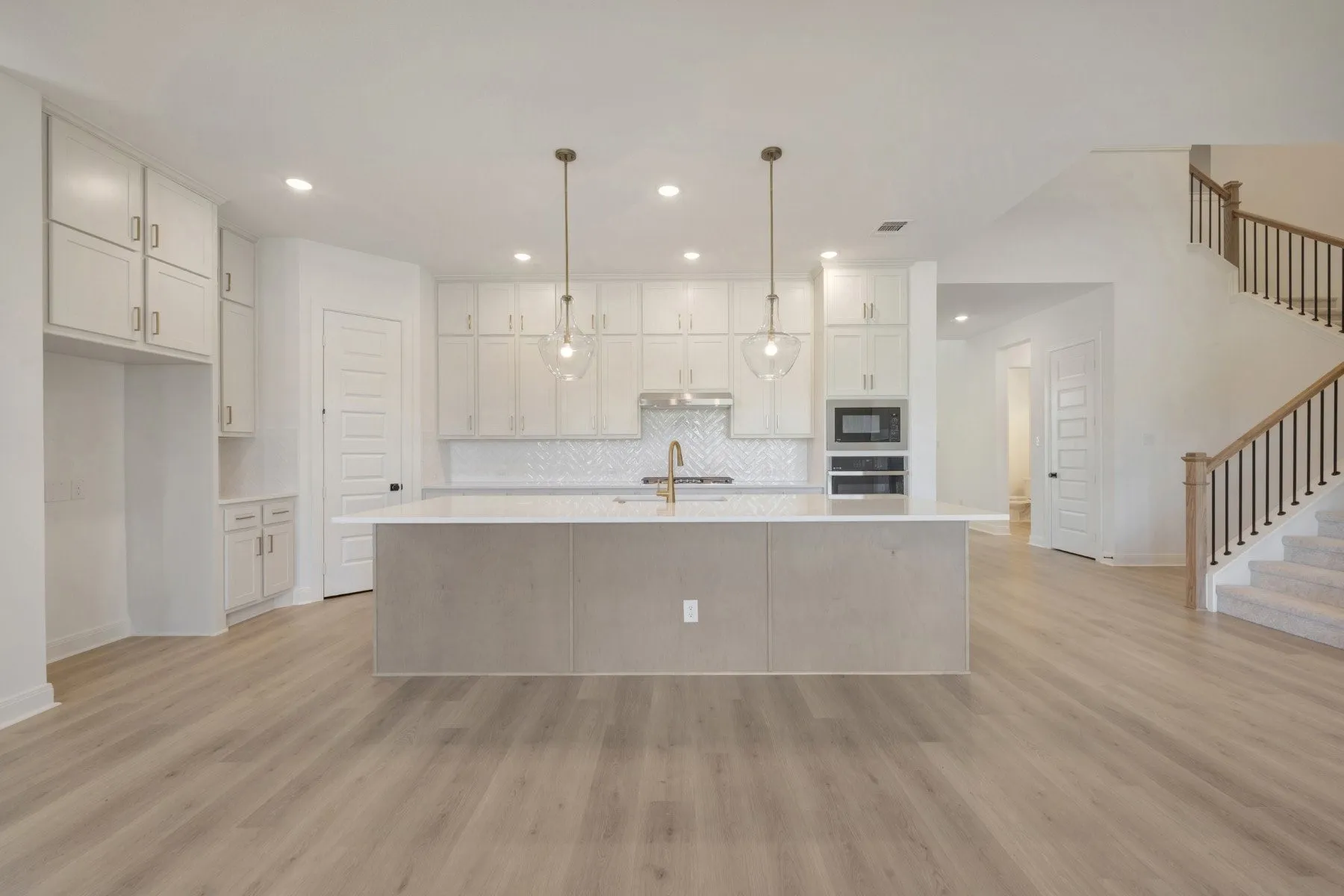 Open-concept kitchen featuring an expansive island with a light-toned countertop, white cabinetry, a herringbone tile backsplash, and recessed lighting