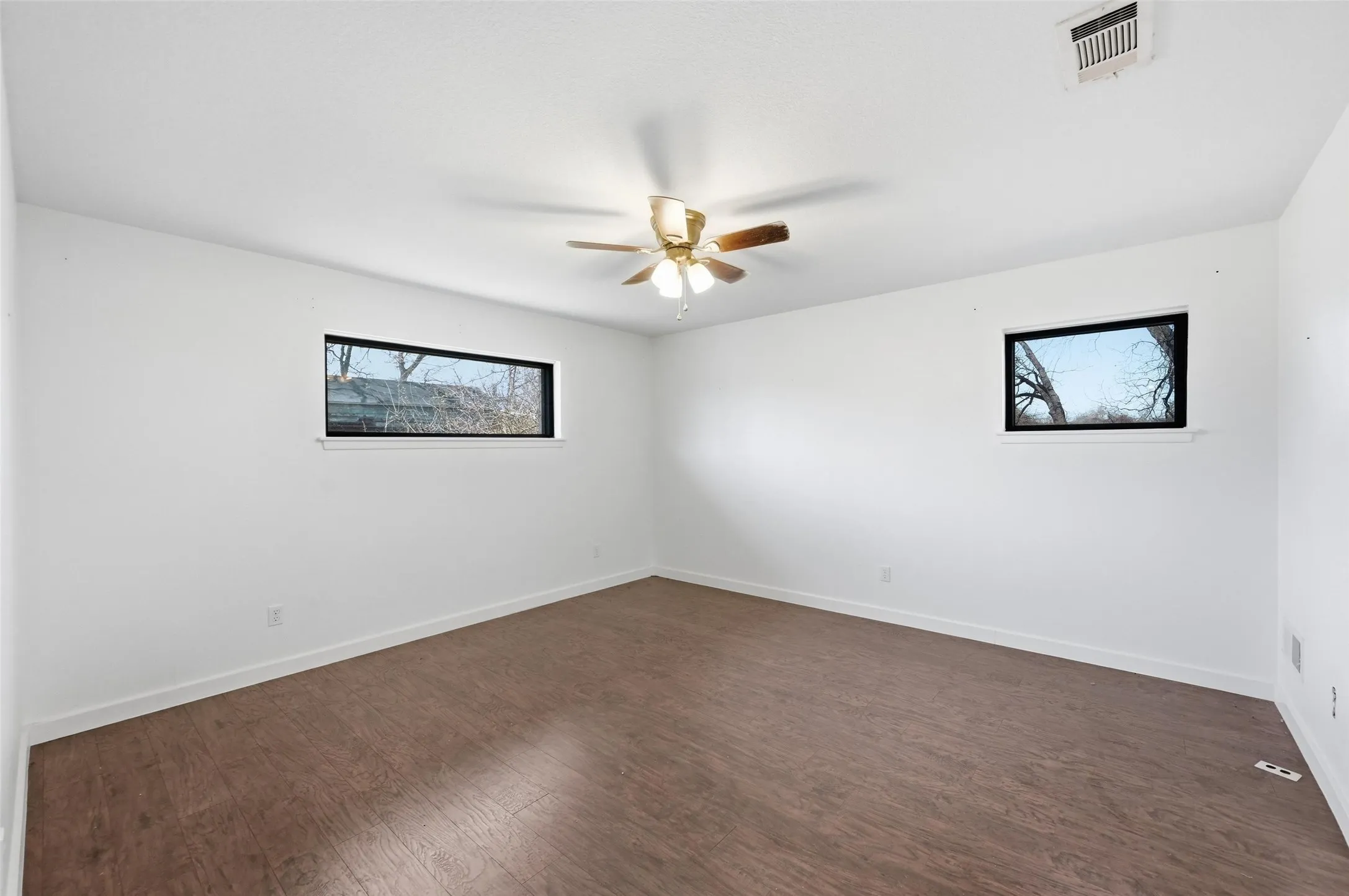 Empty room with dark wood-style floors and a ceiling fan