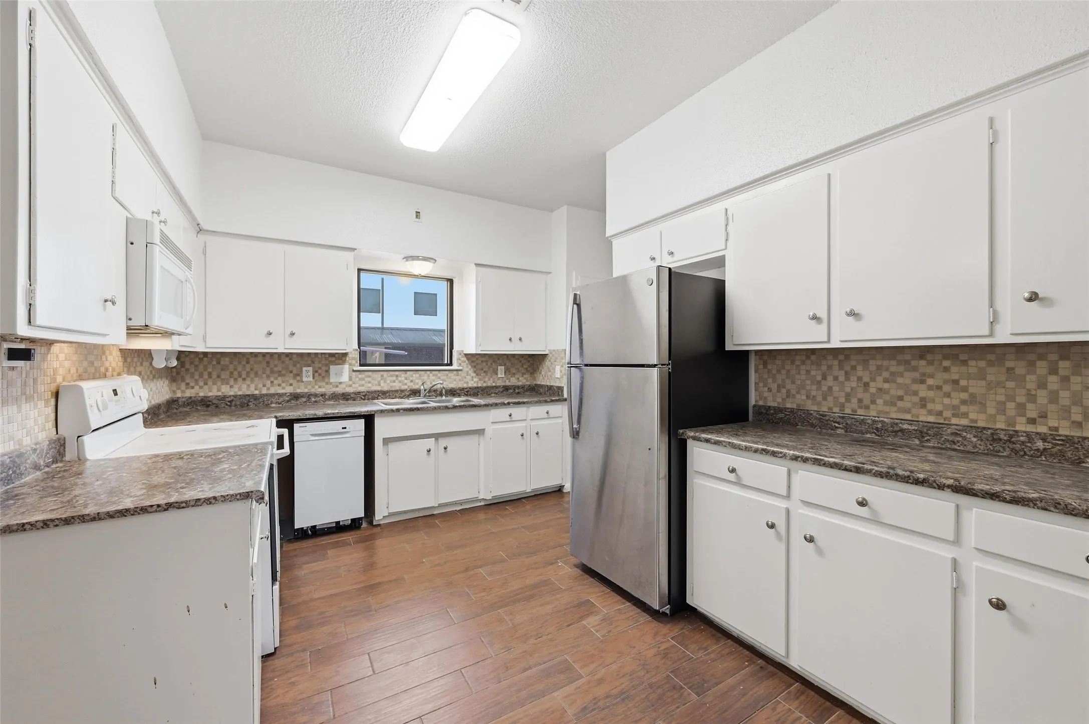 Kitchen with white appliances, white cabinets, dark countertops, dark wood-type flooring, and backsplash
