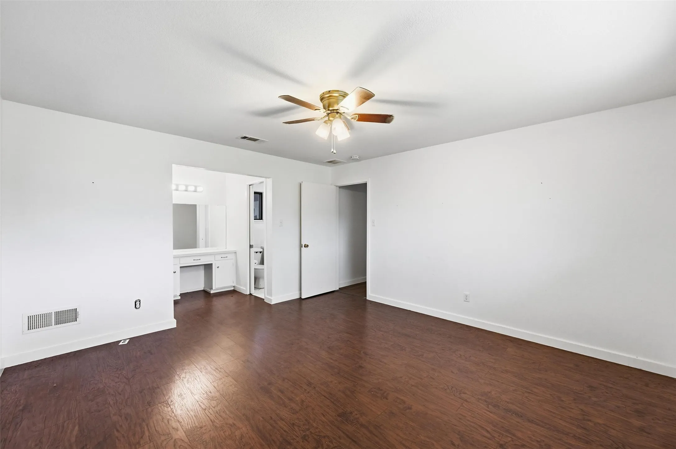 Unfurnished bedroom featuring dark wood-style flooring, an office area, a ceiling fan, and ensuite bathroom