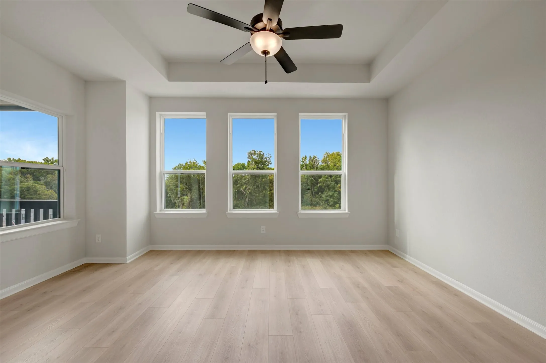 Tray ceiling with a ceiling fan, wood-finish flooring, and multiple windows