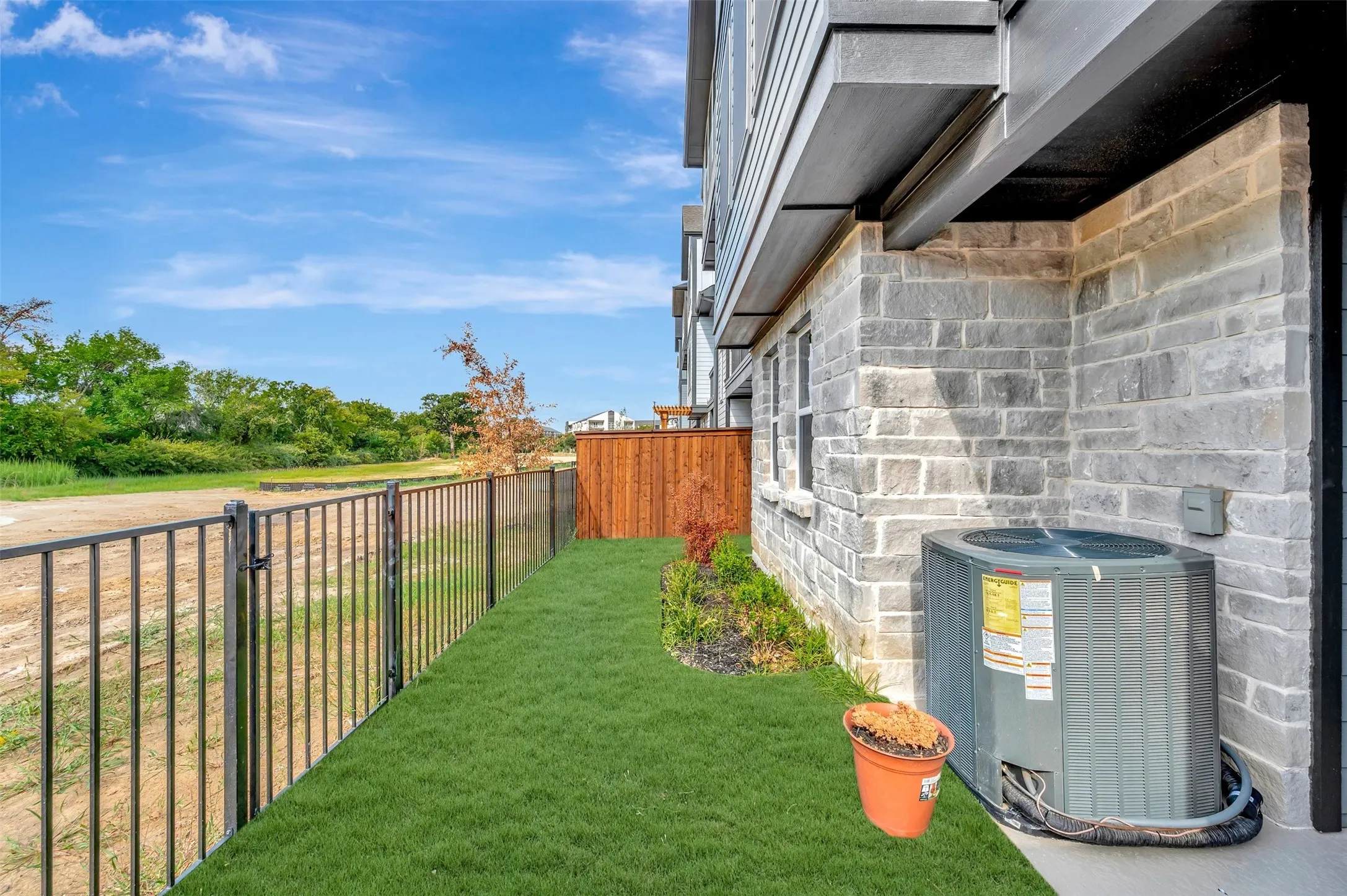 Private outdoor space featuring artificial turf, a metal fence, a wooden privacy fence, and a stone exterior