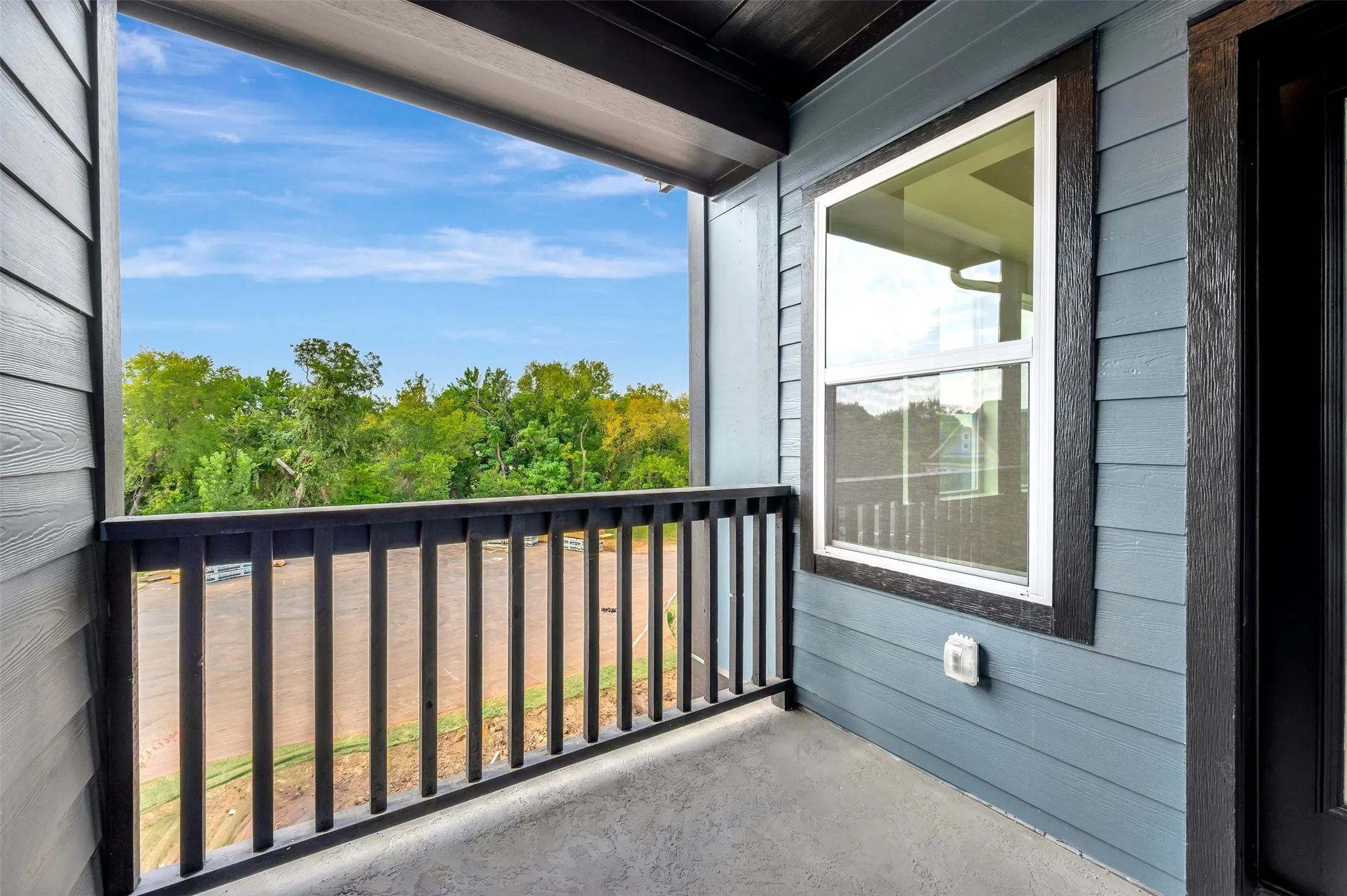 Balcony with a black railing, a window with white trim, and blue siding