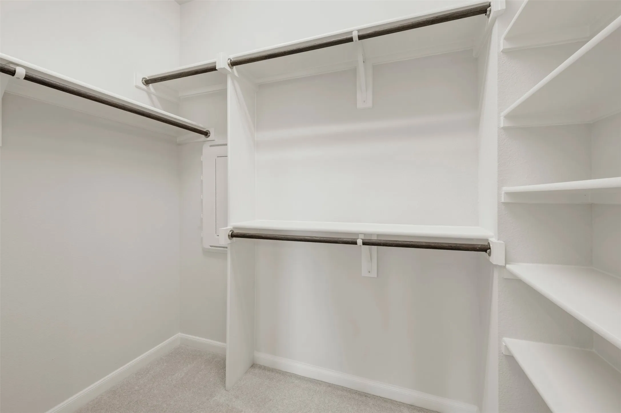 Walk-in closet featuring white built-in shelving, multiple hanging rods, and light-toned carpeting