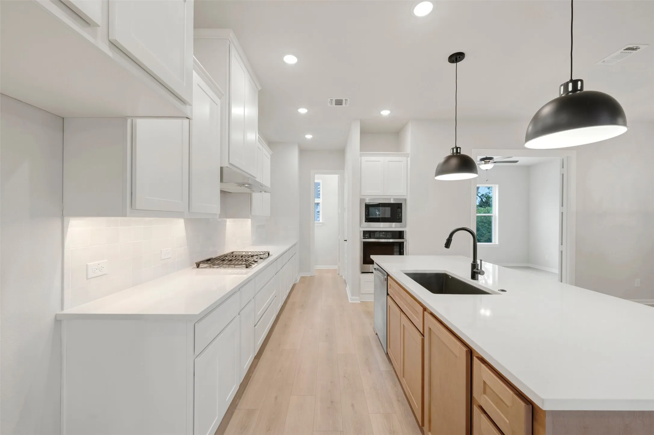 Kitchen featuring white cabinetry, light wood-finish flooring, recessed lighting, a built-in gas range, and an island with a sink and pendant lighting