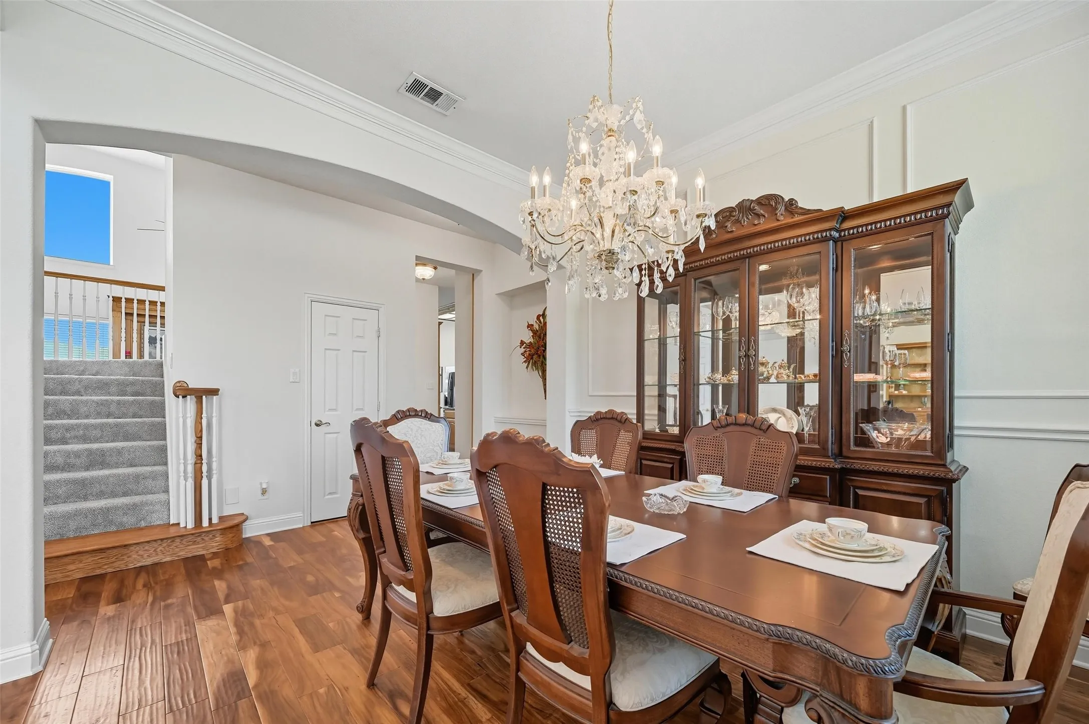 Elegant dining room featuring rich wood flooring, a stunning glass chandelier, and graceful arched architectural details.