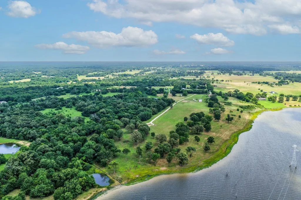 Expansive waterfront property featuring a substantial tree line, open green spaces, and a private pond