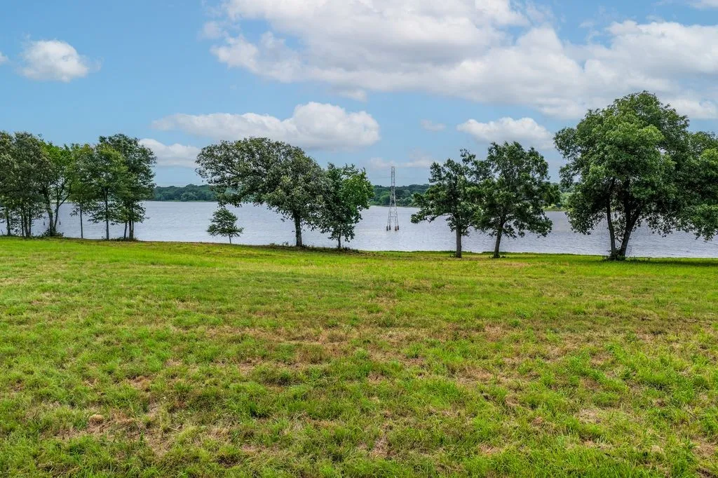 Expansive green lawn with water frontage, mature trees lining the shore, and open water extending to the horizon