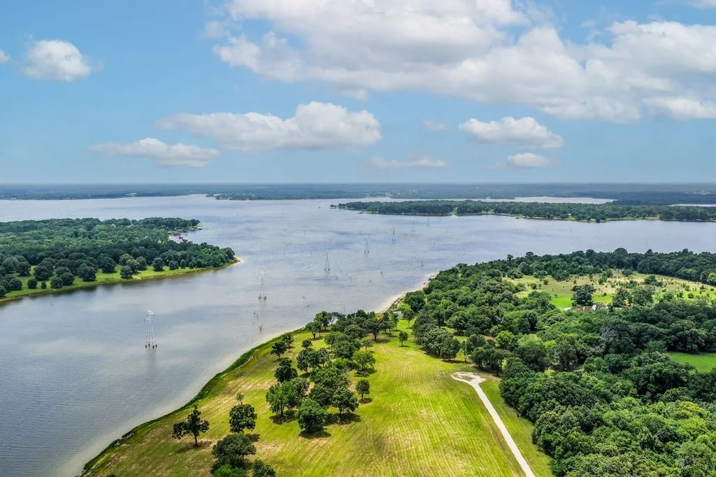 Expansive waterfront property featuring a large body of water, lush green tree lines, and open grassy areas
