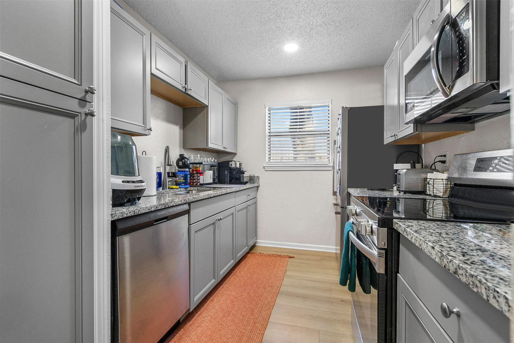 Kitchen with stainless steel appliances, gray cabinetry, a textured ceiling, light wood-style flooring, and light stone counters
