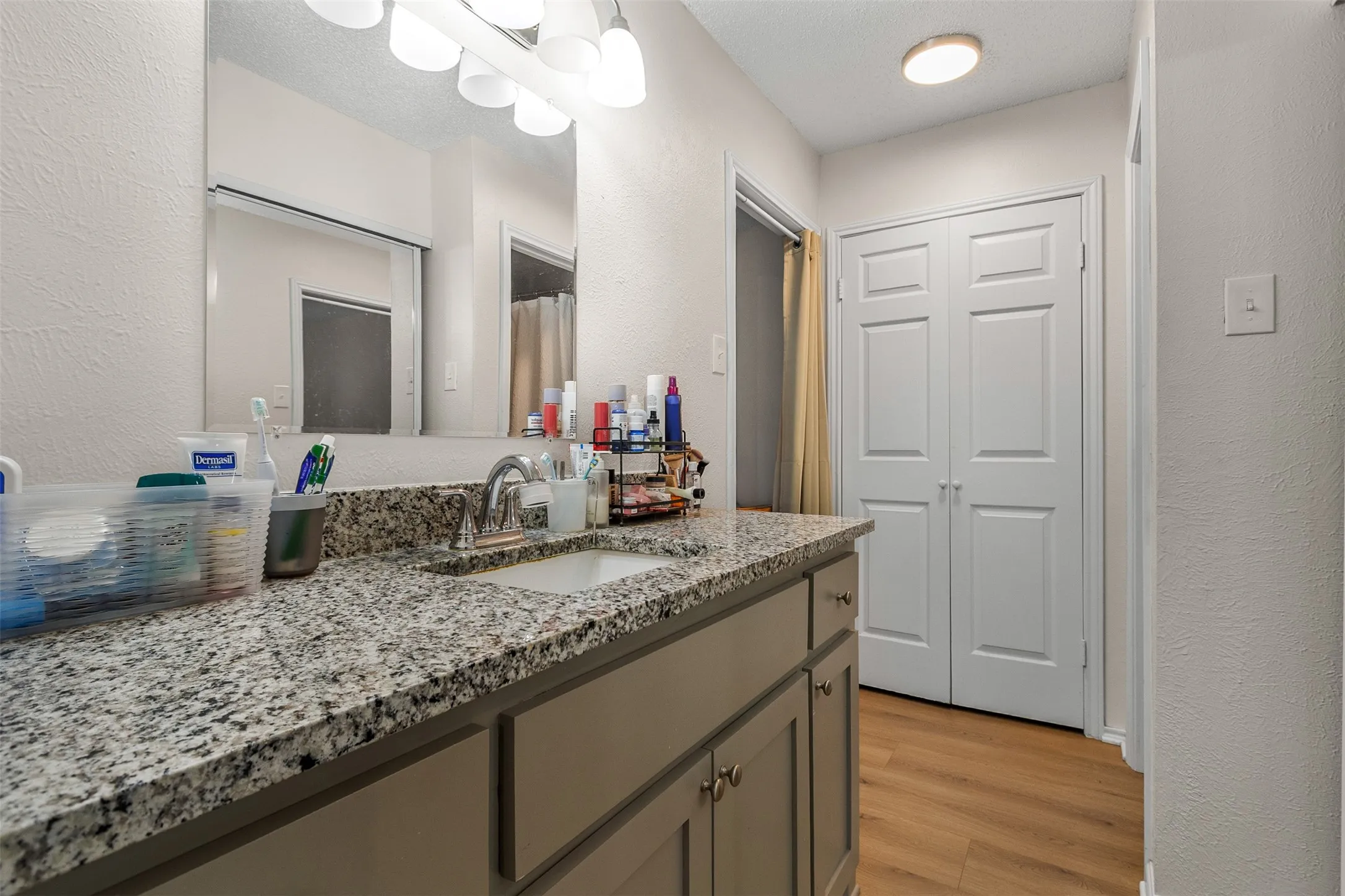 Full bath with a textured wall, vanity, light wood-type flooring, and a shower with shower curtain