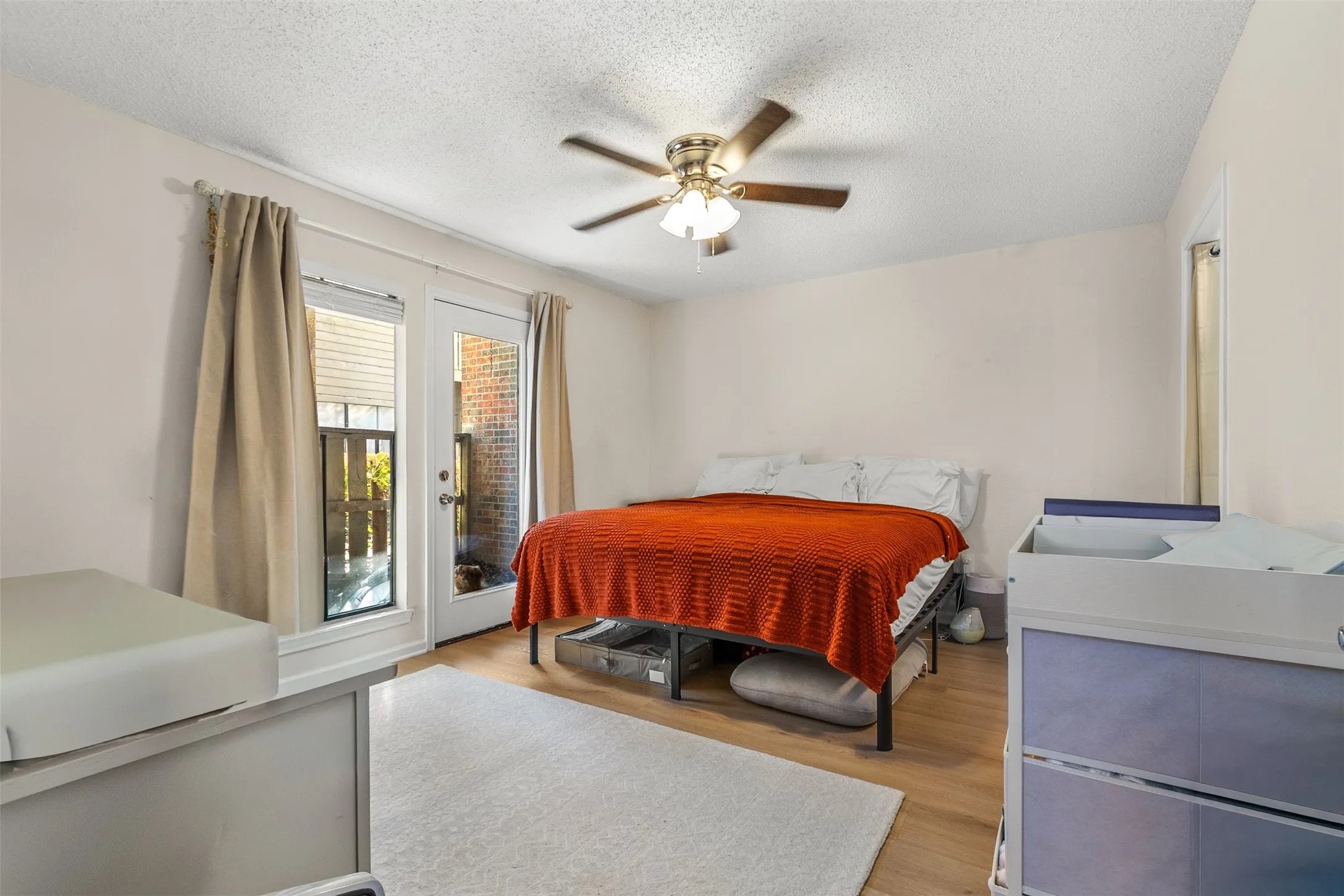 Bedroom with access to exterior, light wood-style flooring, ceiling fan, and a textured ceiling