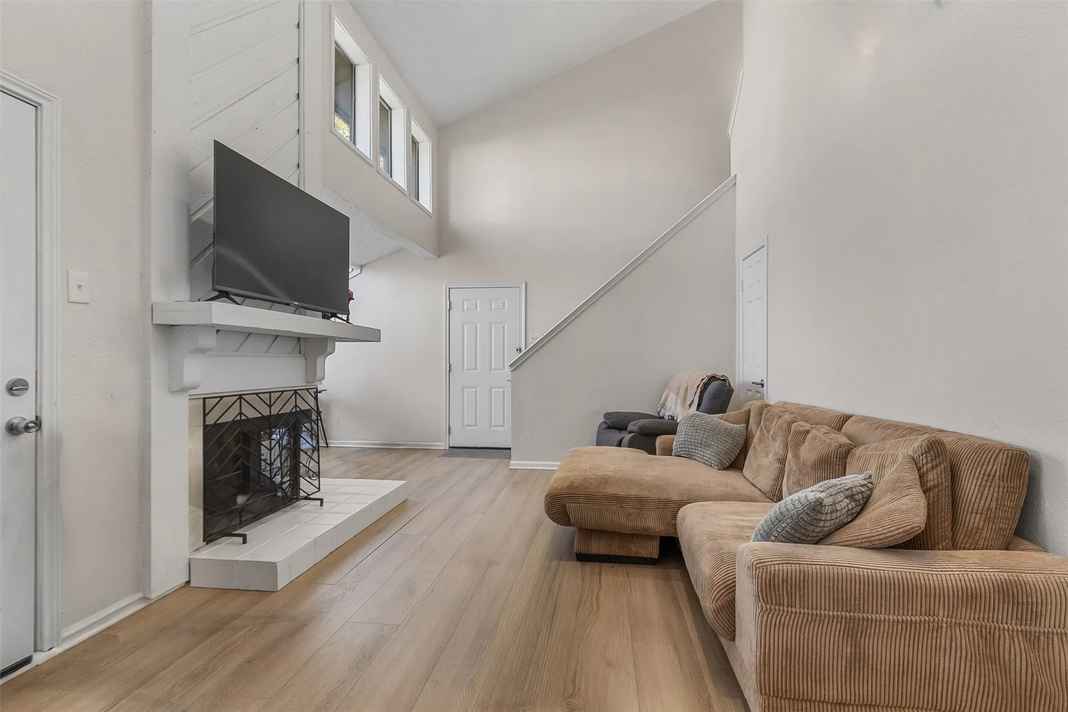 Living area with light wood-style floors, a tiled fireplace, and lofted ceiling