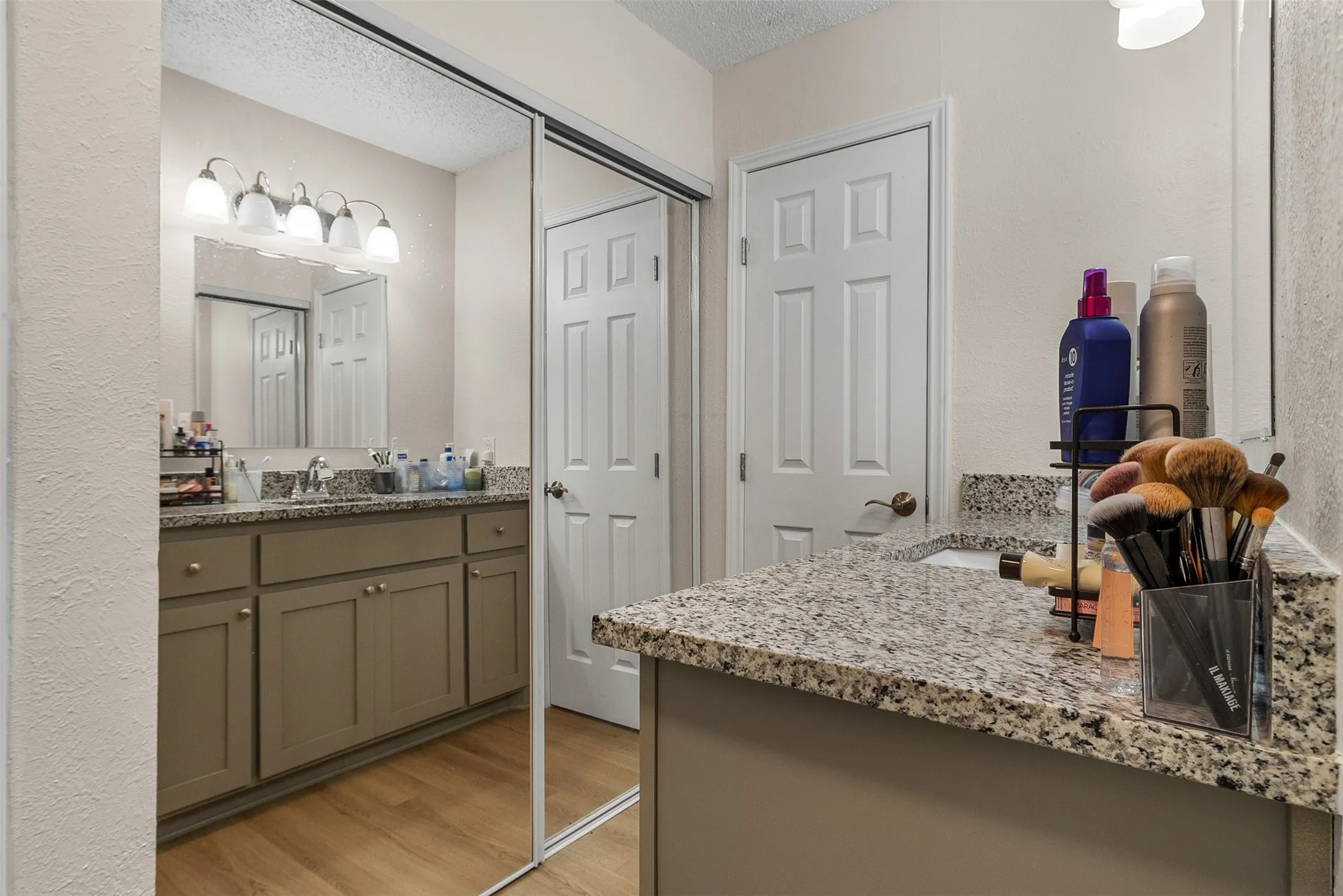Full bath with light wood-style floors, two vanities, a textured wall, and a textured ceiling