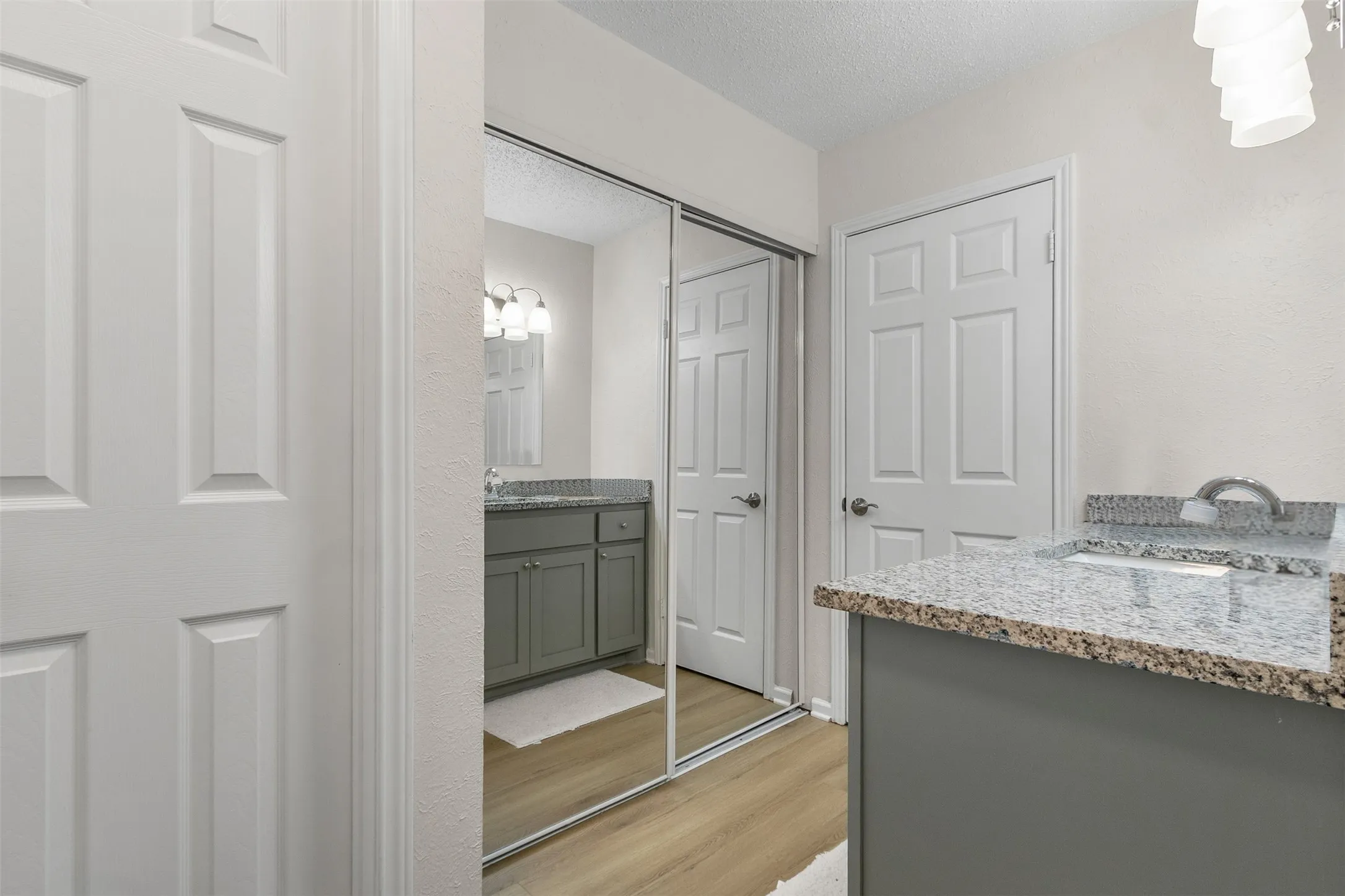 Full bath with two vanities, light wood-style flooring, and a textured ceiling