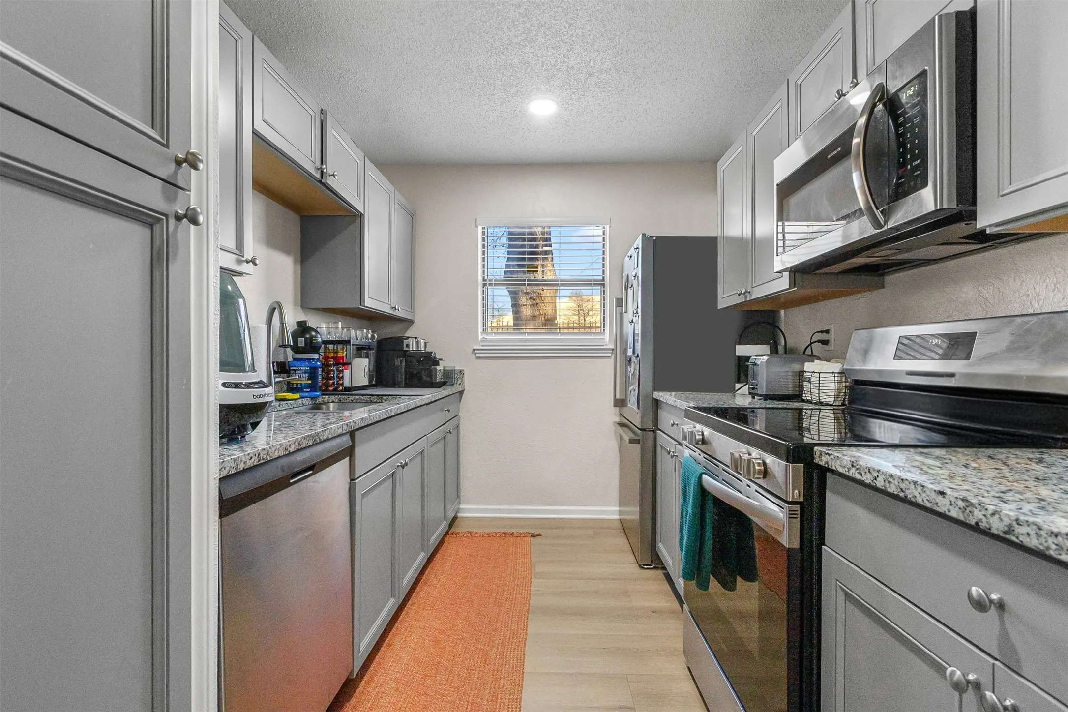 Kitchen featuring stainless steel appliances, gray cabinets, a textured ceiling, light wood-style floors, and light stone countertops