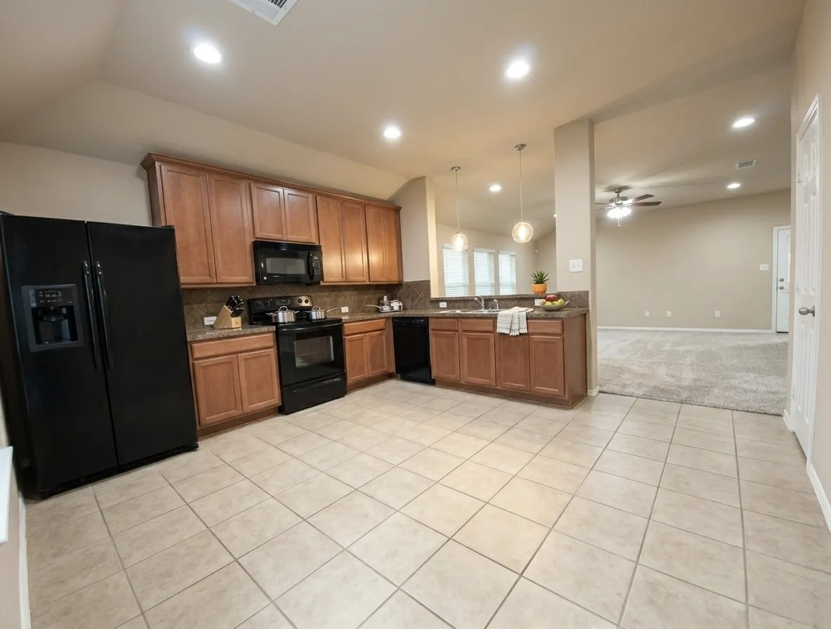 Kitchen featuring black appliances, wood finish cabinets, light tile patterned flooring, light colored carpet, and hanging light fixtures