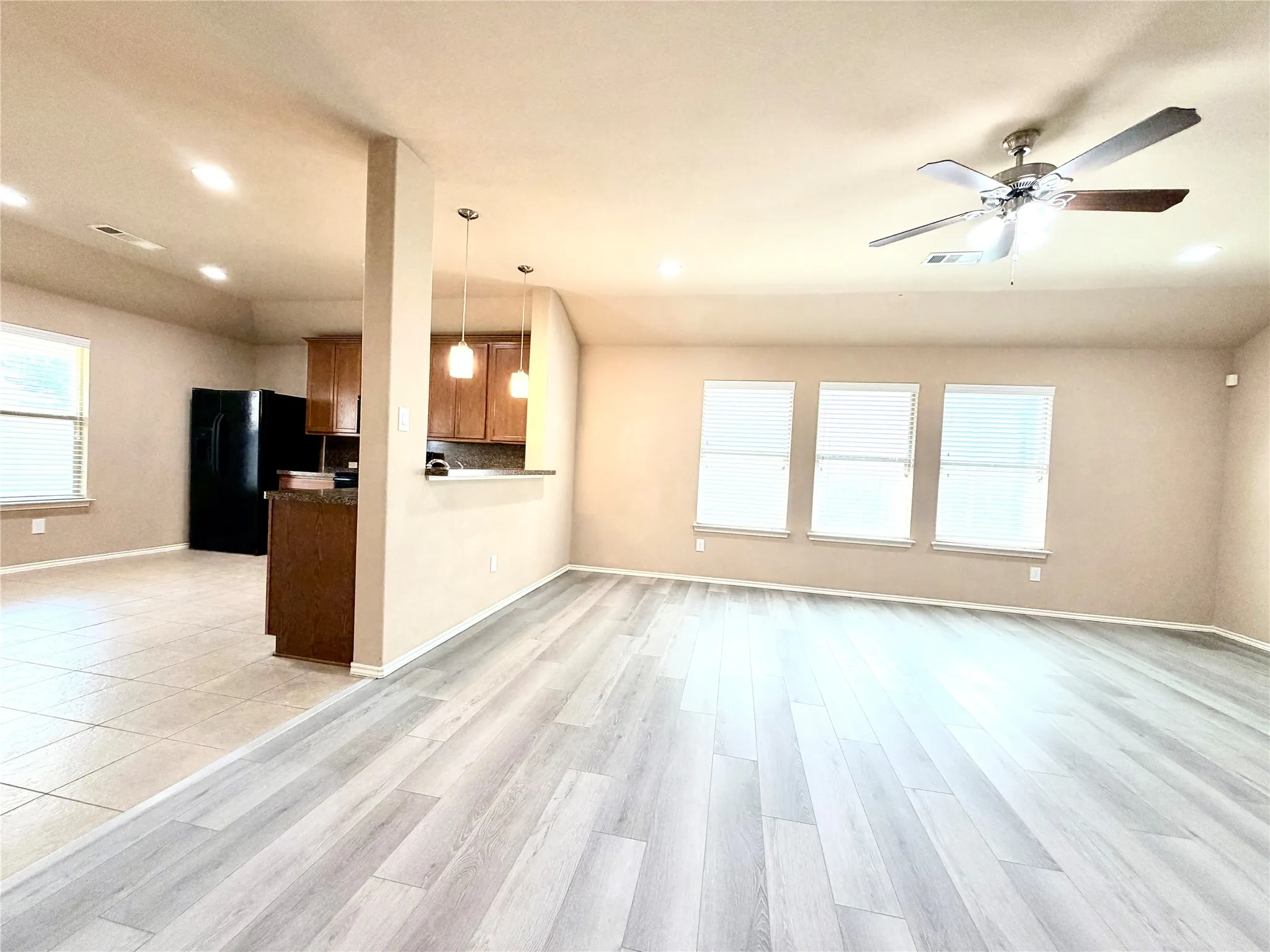 Spacious living area featuring light wood-finish flooring, a ceiling fan, and three windows with blinds
