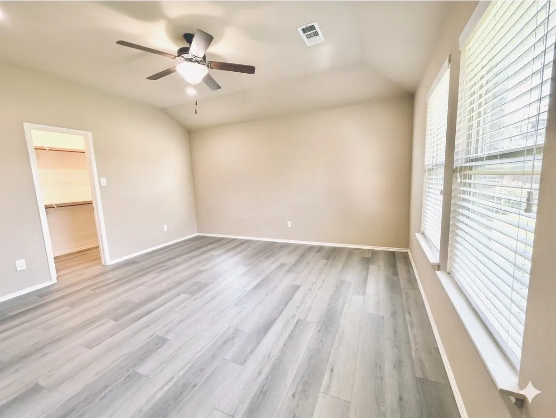 Spacious room featuring vaulted ceilings, light gray wood-finish flooring, and a ceiling fan with light fixture