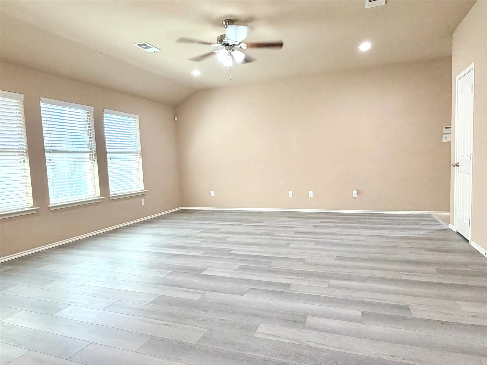 Spacious room featuring vaulted ceilings, recessed lighting, a ceiling fan, light wood-finish flooring, and multiple windows with blinds
