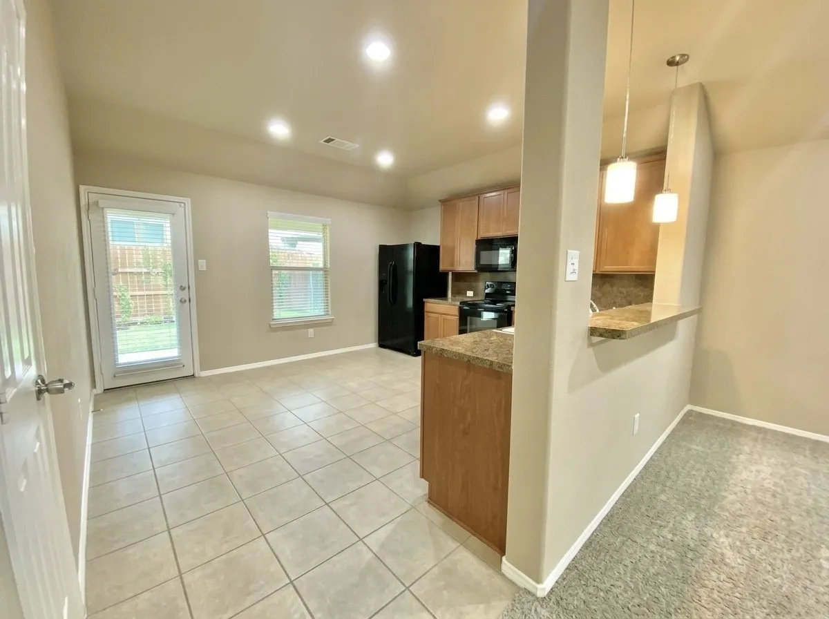 Kitchen featuring black appliances, light tile patterned floors, hanging light fixtures, light carpet, and a peninsula