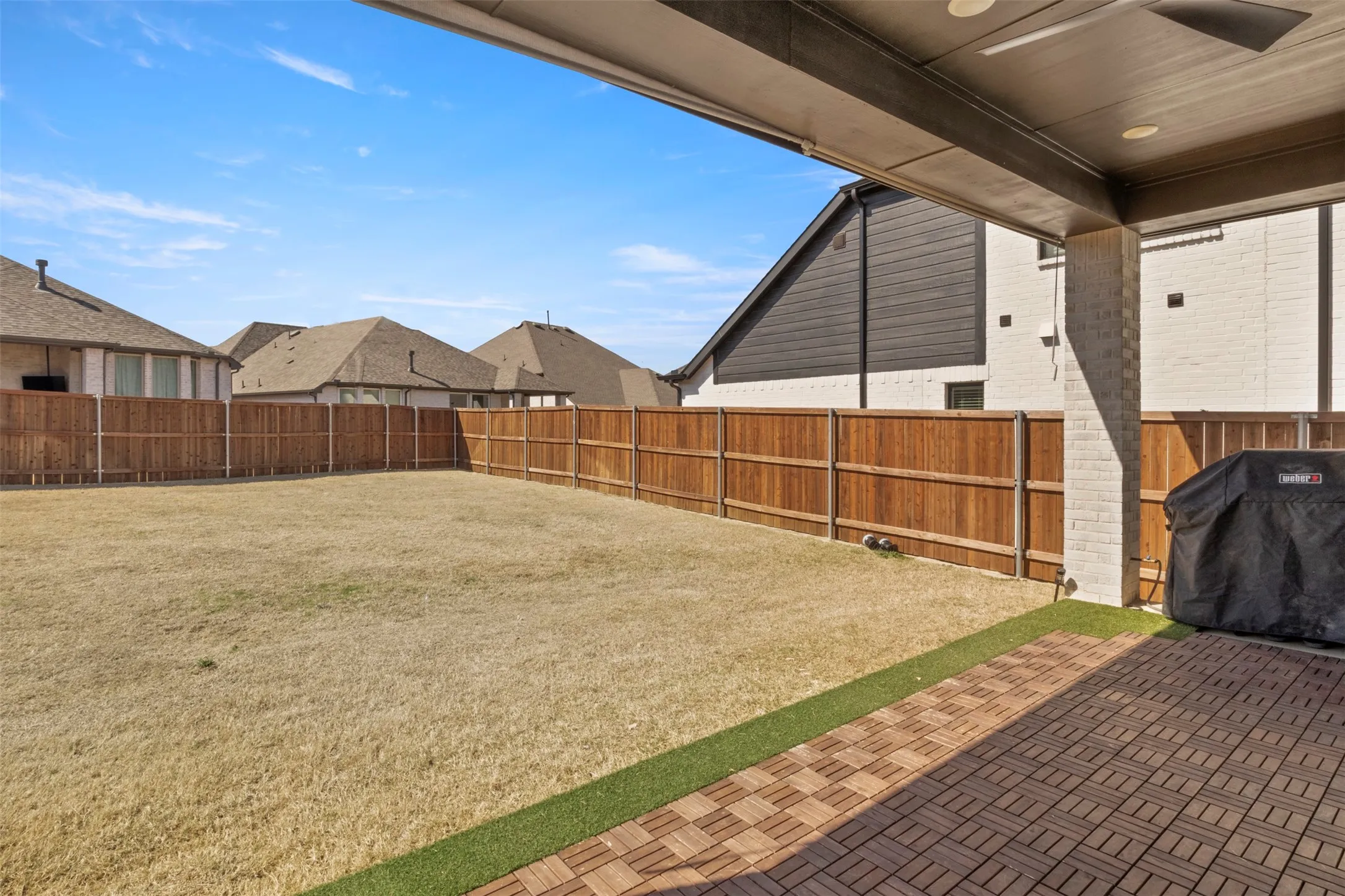 Spacious backyard featuring a covered patio with recessed lighting, a ceiling fan, and brick-look paver flooring